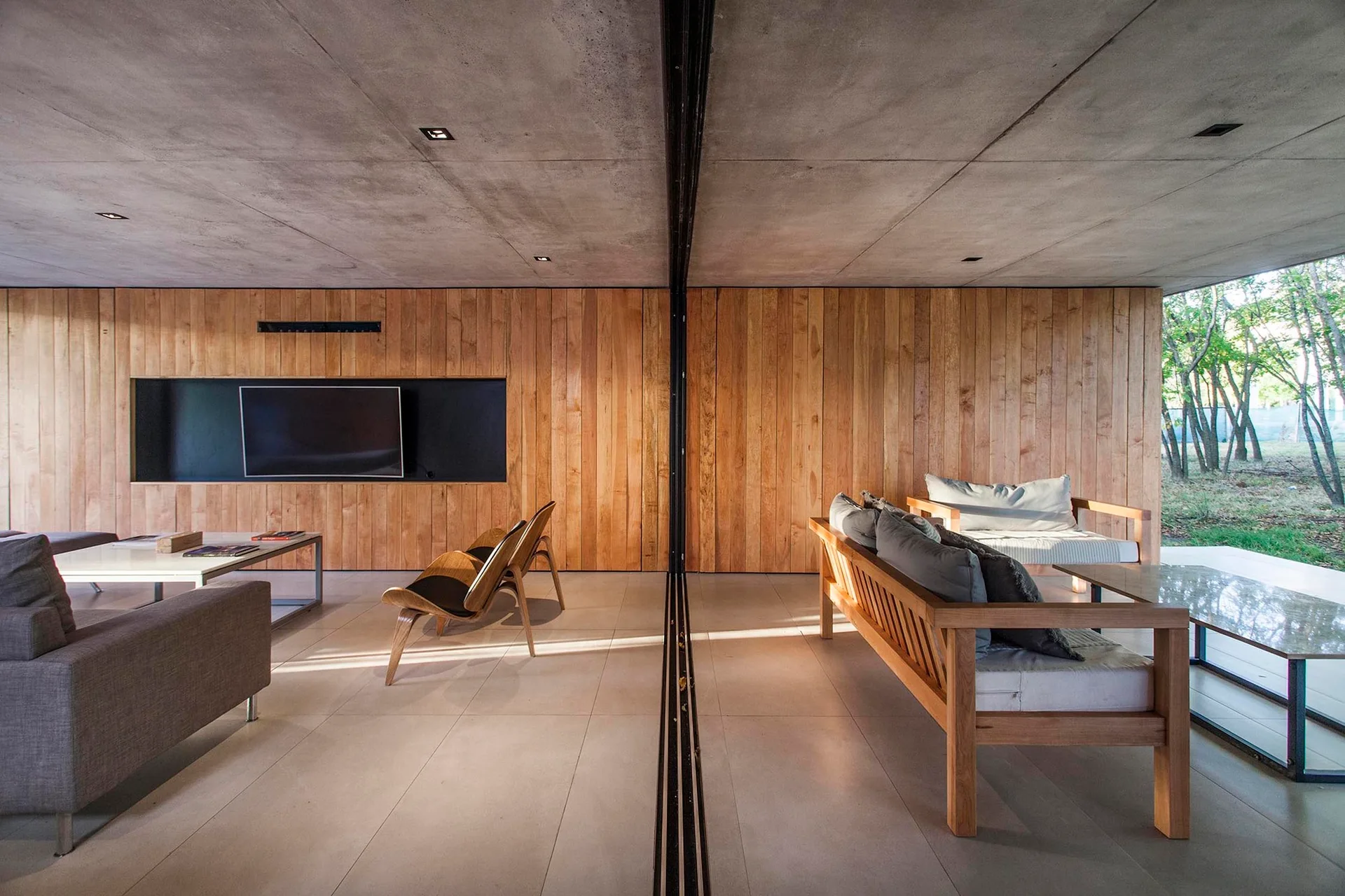 A modern living area features vertical wood paneling, an exposed concrete ceiling, a recessed television niche, and contemporary furniture.