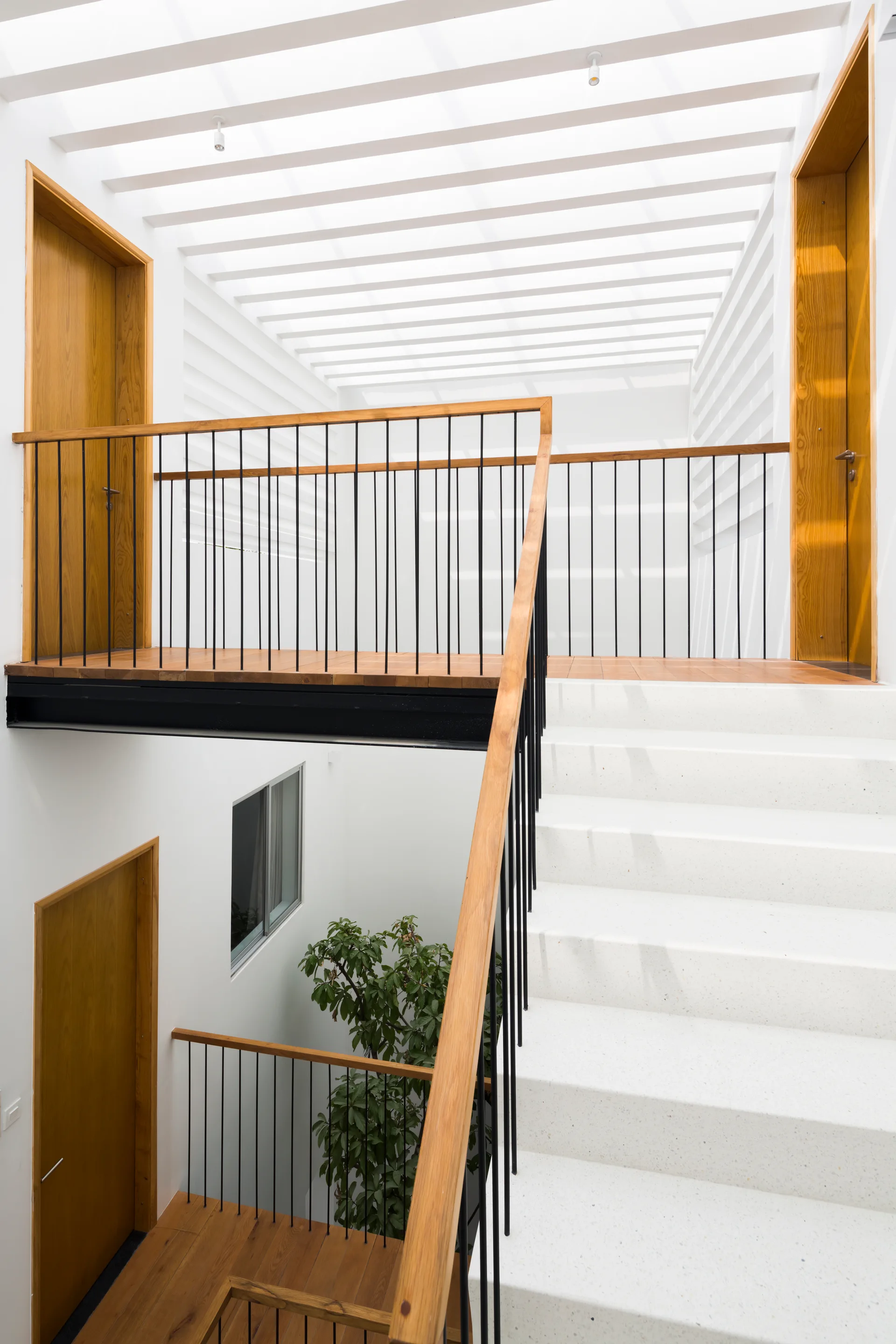A modern white staircase with stone-textured steps, black metal railings, warm wood handrails, and wood doors under a slatted ceiling.