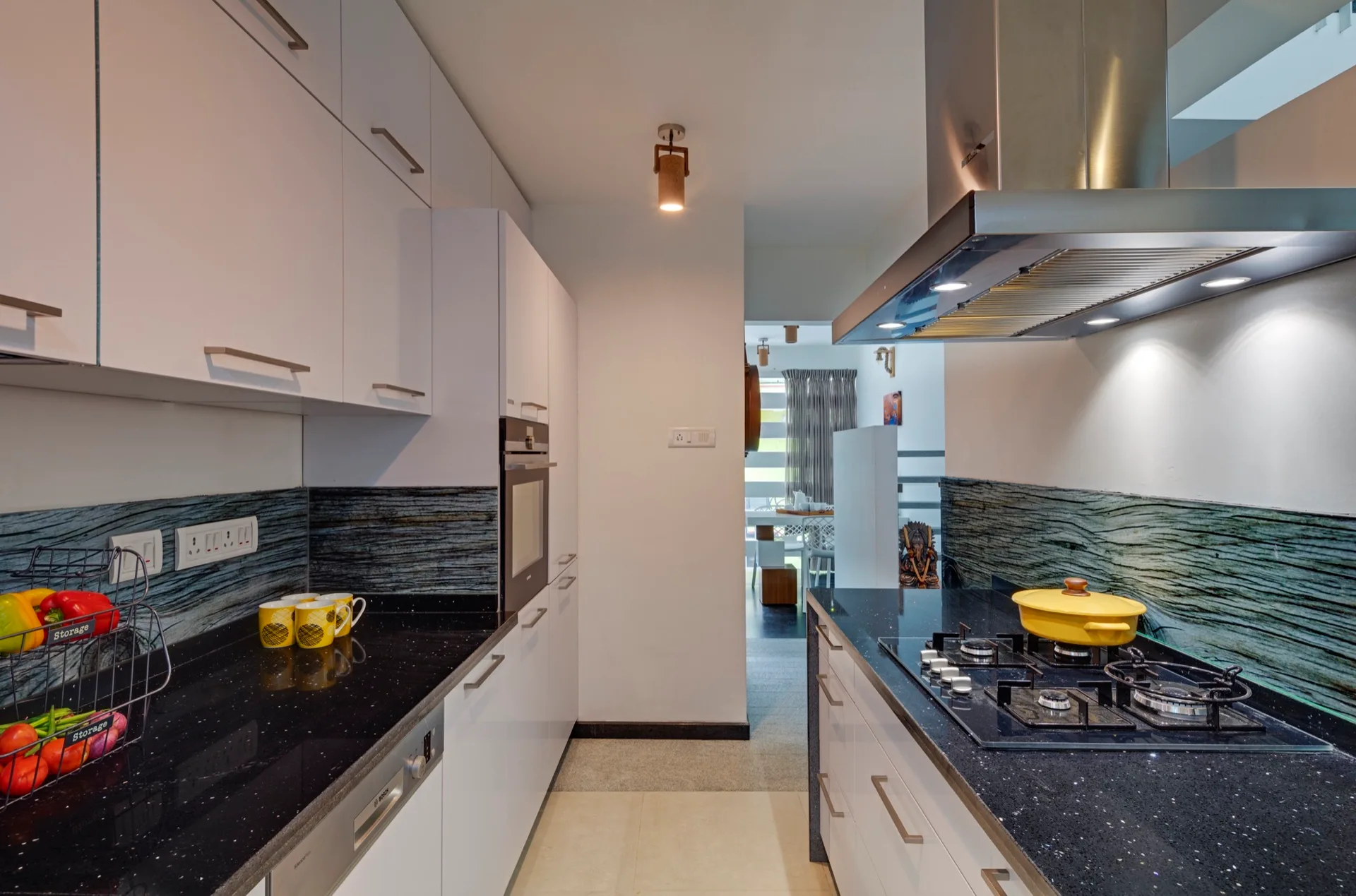 A modern galley kitchen features glossy white cabinets, black flecked countertops, a gas cooktop, and a textured green glass backsplash.