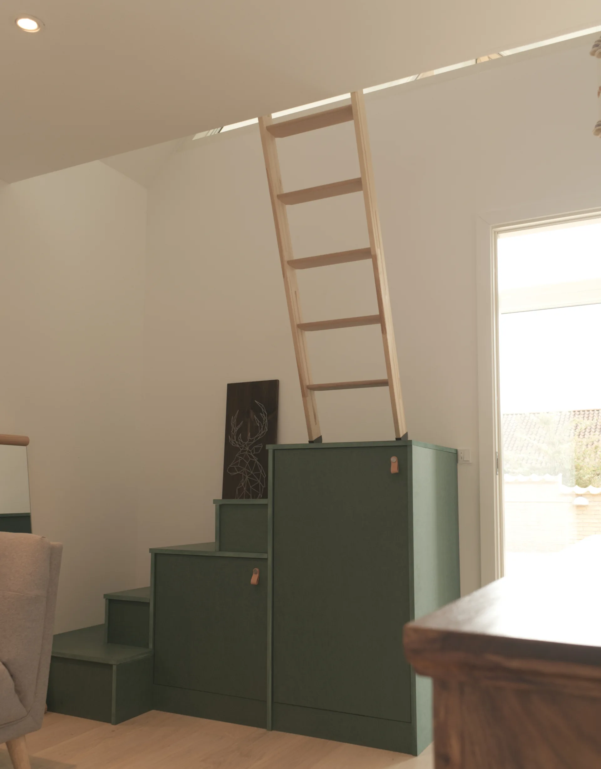 A muted green storage cabinet built as staircase steps supports a light wood ladder leading to a loft opening.