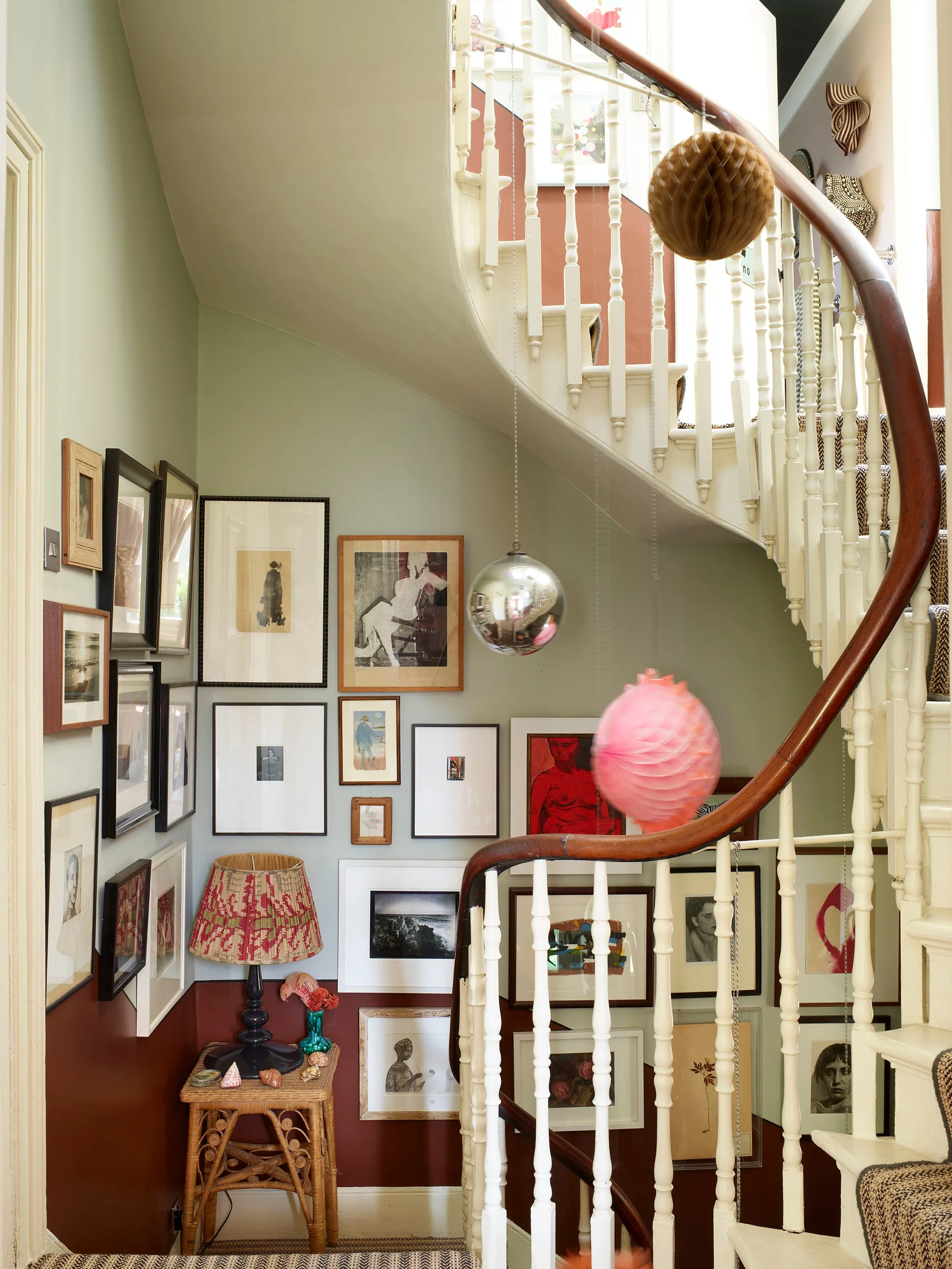 A curved staircase with a wooden handrail features a dense gallery wall of framed art on sage green and dark red painted walls.