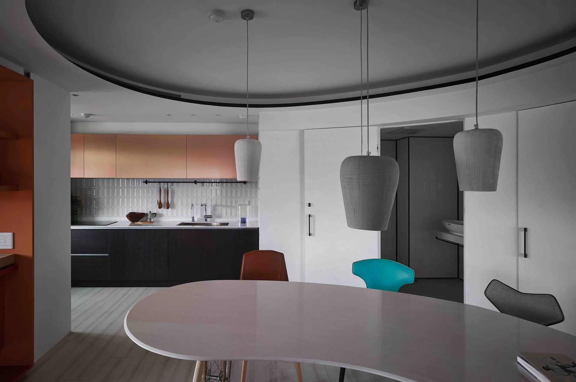 A modern open-concept kitchen and dining area with metallic copper upper cabinets, dark lower cabinets, and a white curved dining table.