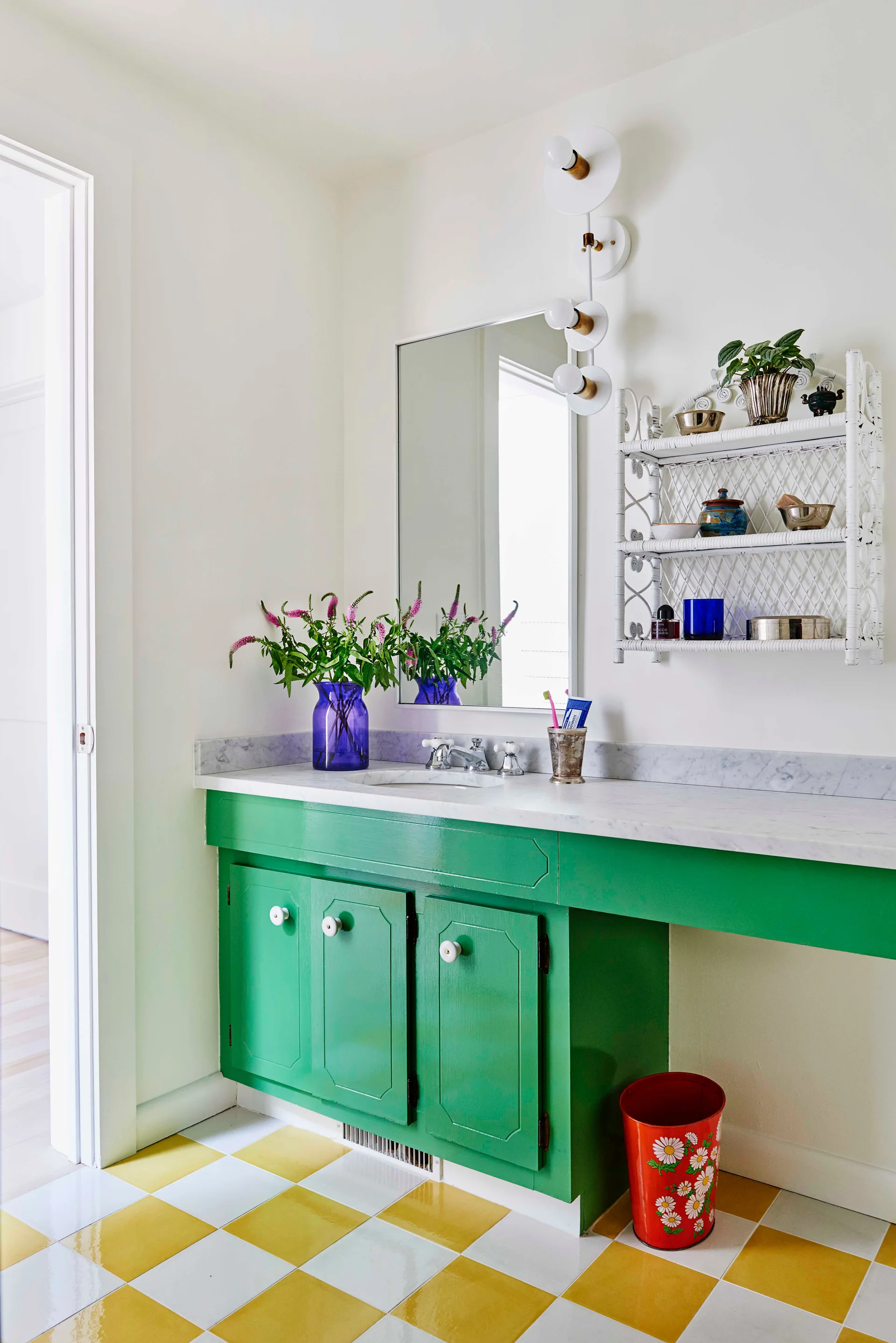 A bathroom features a glossy green vanity with a marble countertop, yellow and white checkerboard floor tiles, and a white wicker wall shelf.