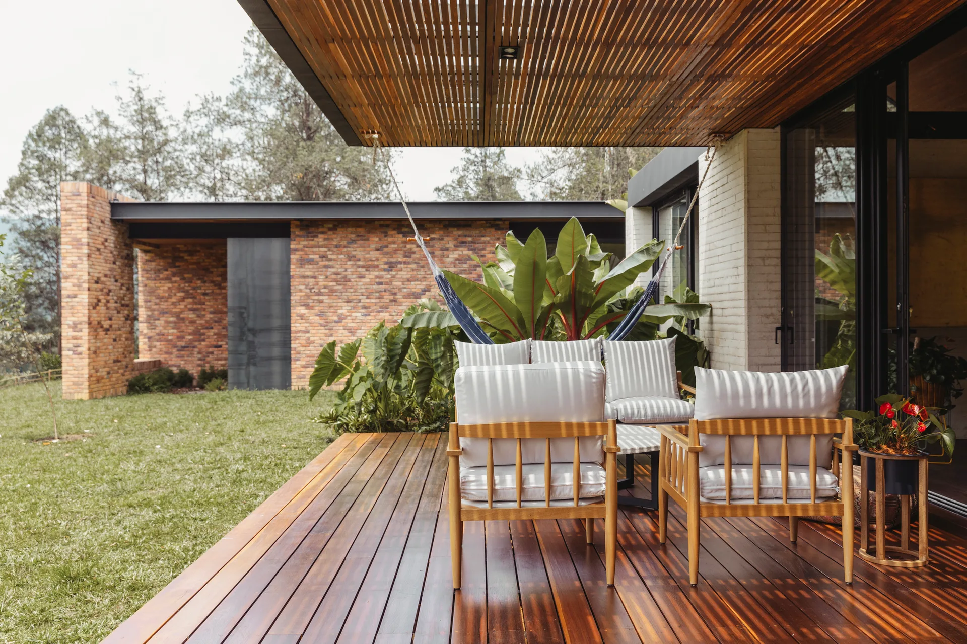A wooden patio deck features lounge chairs with striped cushions and a hanging hammock under a slatted wood ceiling overhang.