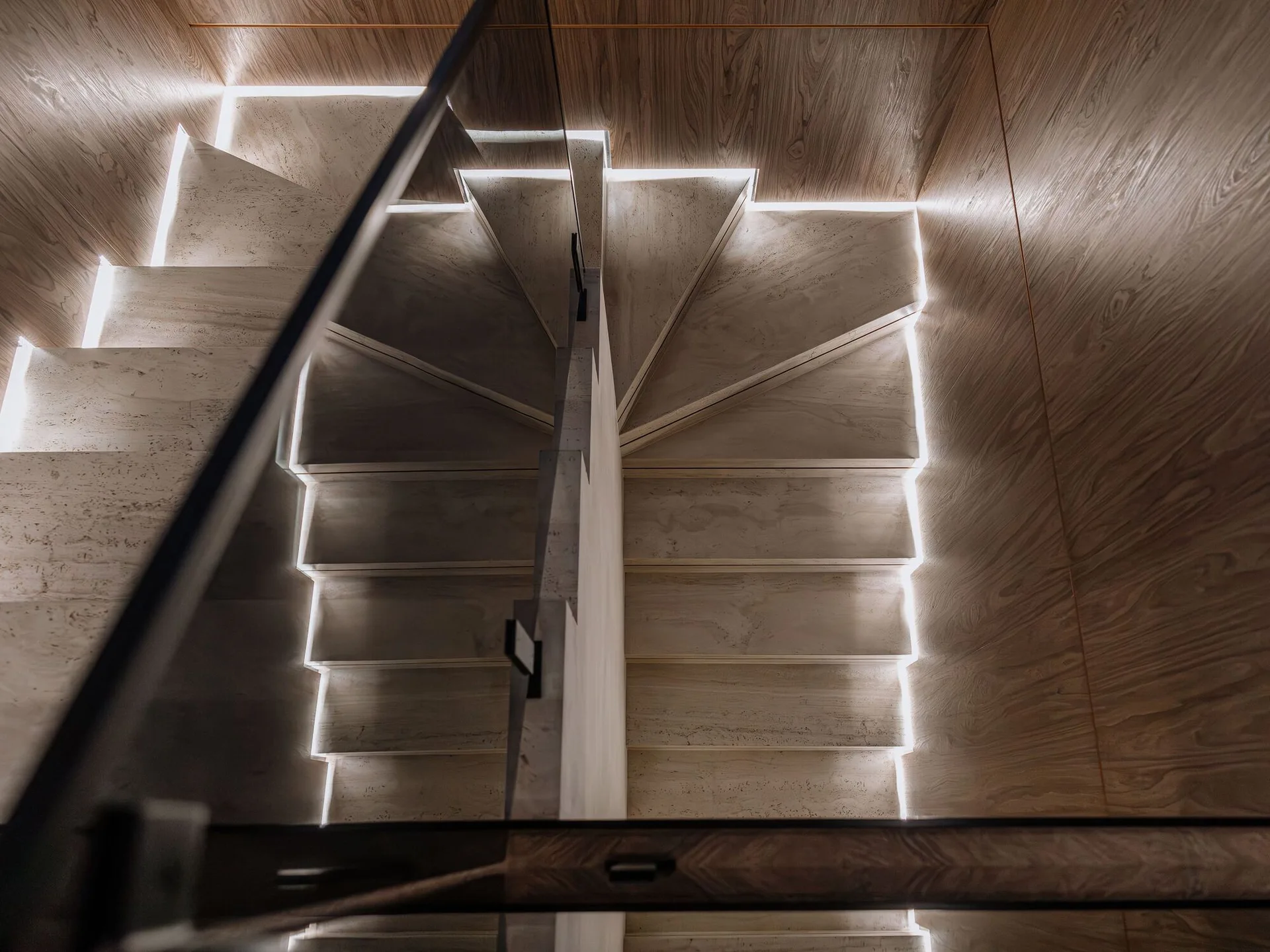A modern staircase features textured stone-like treads outlined with glowing LED strip lights against wood-grain paneled walls.