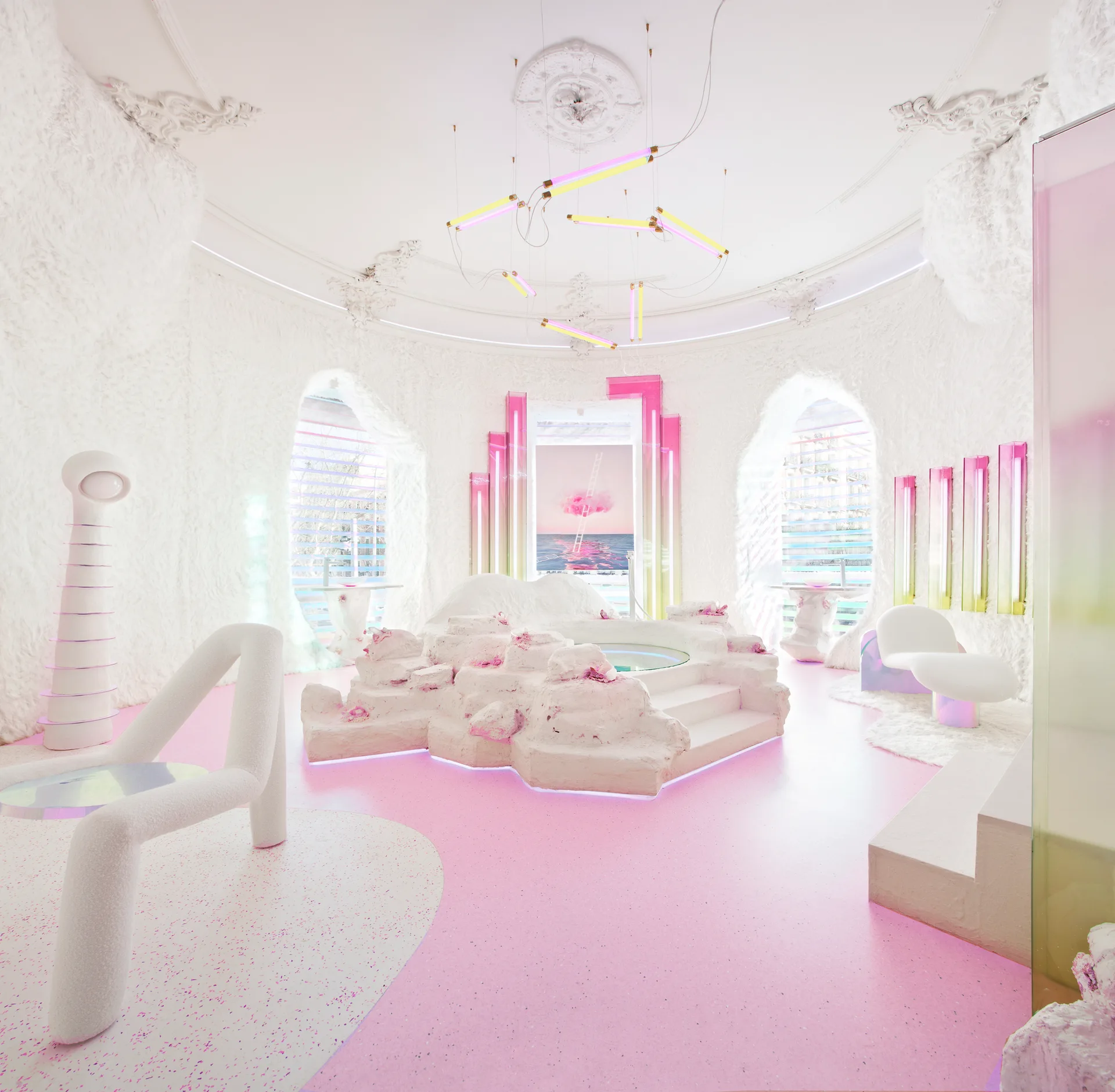 A surreal lounge features a central rock-like seating platform, a speckled pink floor, and glowing neon light fixtures beneath an ornate ceiling.