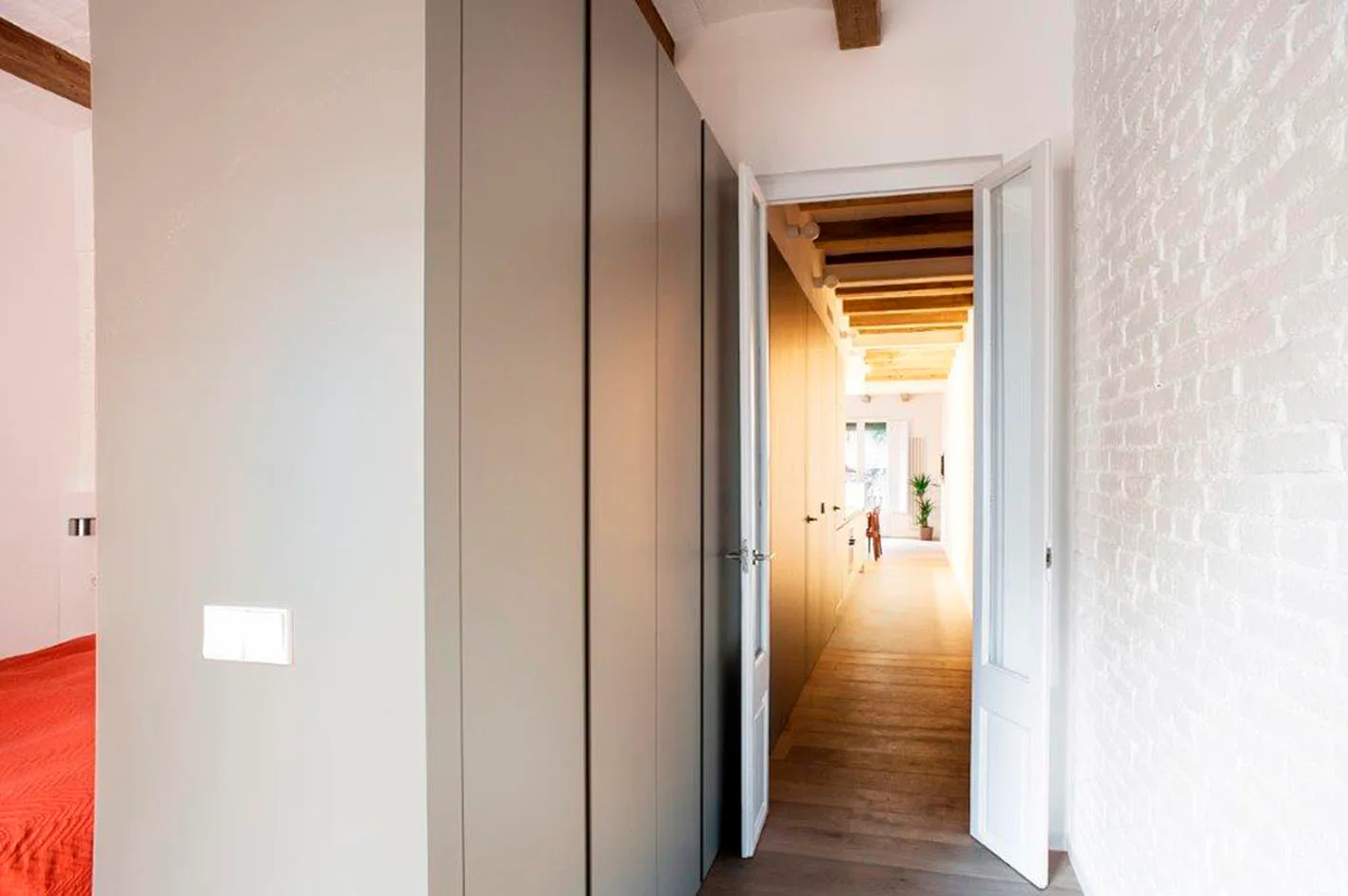 A long hallway features tall matte grey cabinets, a white painted brick wall, hardwood floors, and exposed wooden ceiling beams.