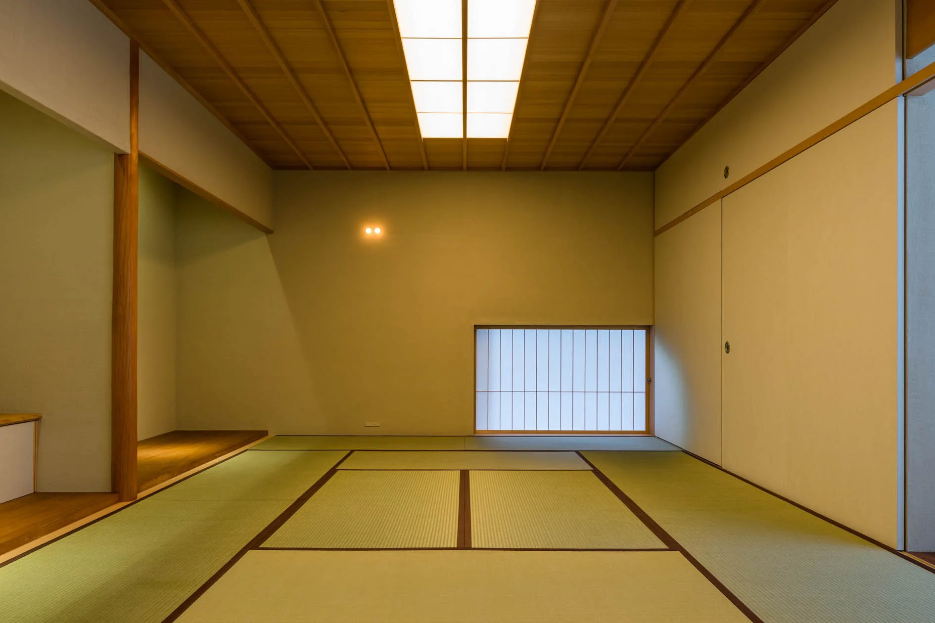A minimalist Japanese room features tatami mat flooring, a low shoji screen window, sliding paper doors, and a glowing wood-framed ceiling light.