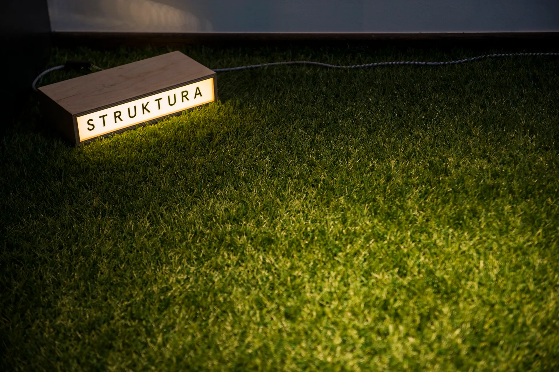 A rectangular wooden light box with glowing text rests on a surface of green artificial grass.