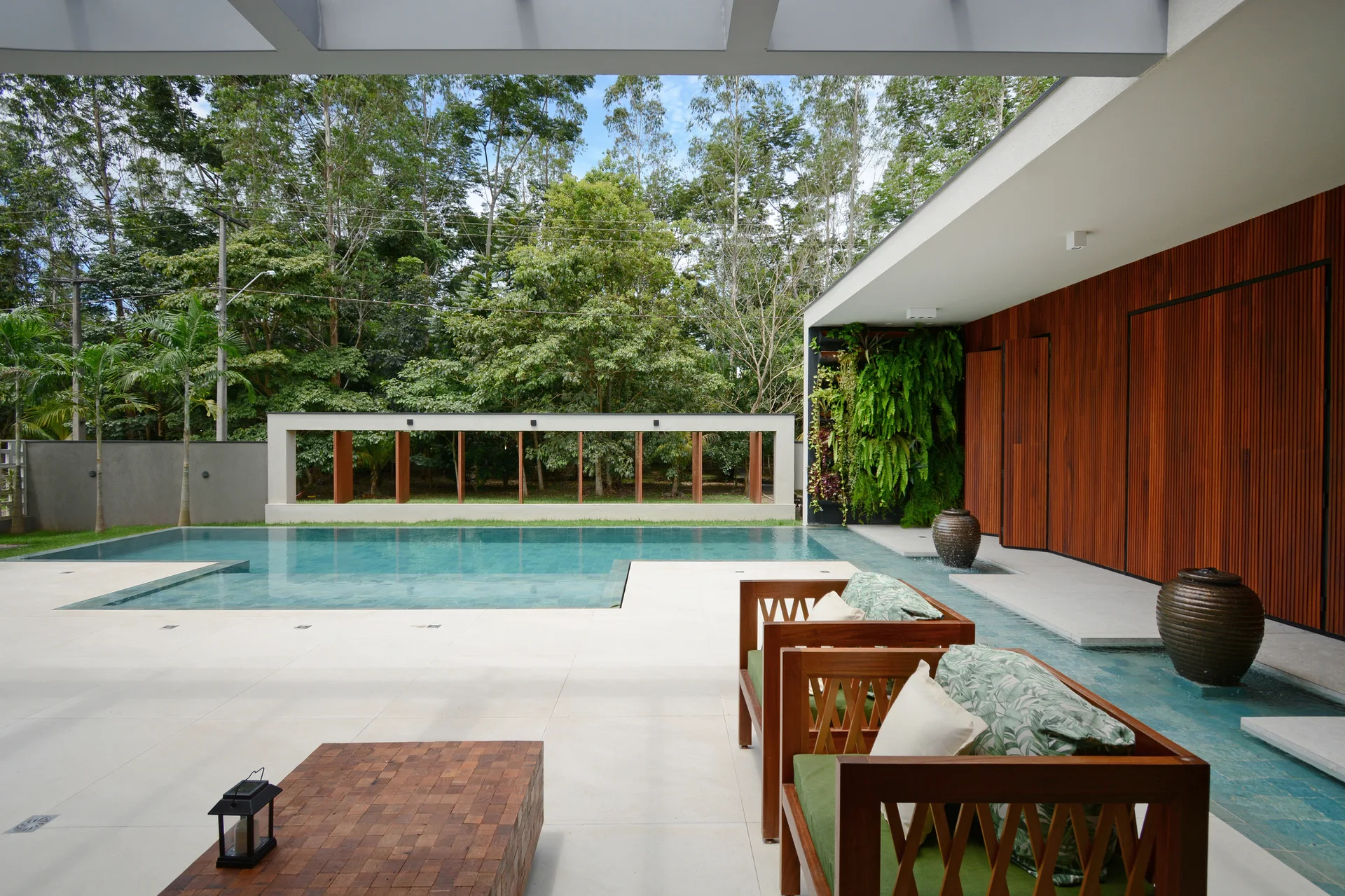 A modern outdoor pool patio features wooden lounge chairs, a rectangular swimming pool, a vertical garden wall, and rich wood-slat paneling.