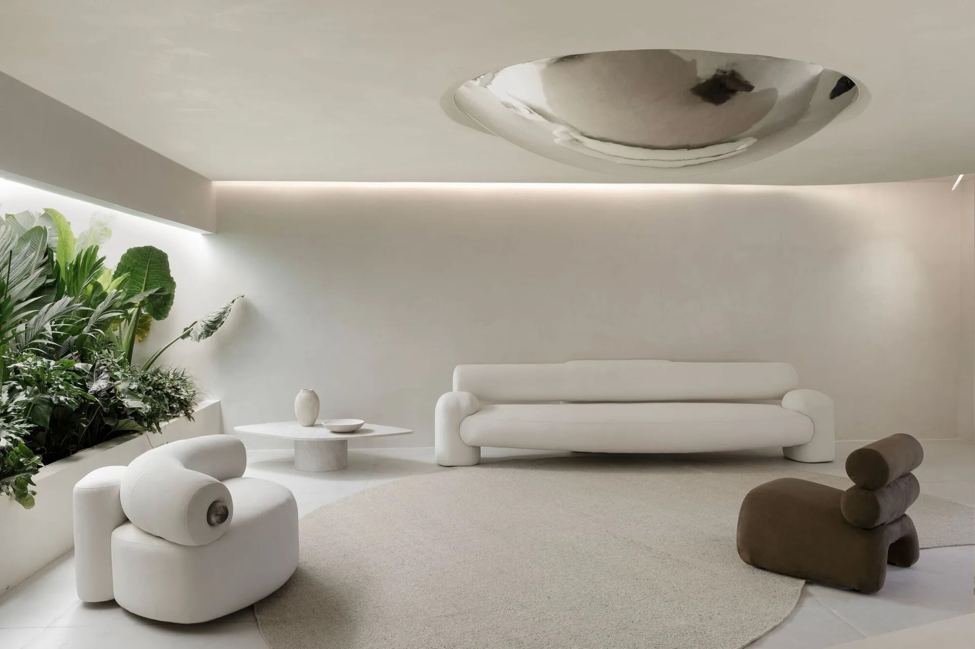 A minimalist off-white living room featuring a curved cream sofa, a circular rug, a built-in planter with green plants, and a metallic ceiling dome.