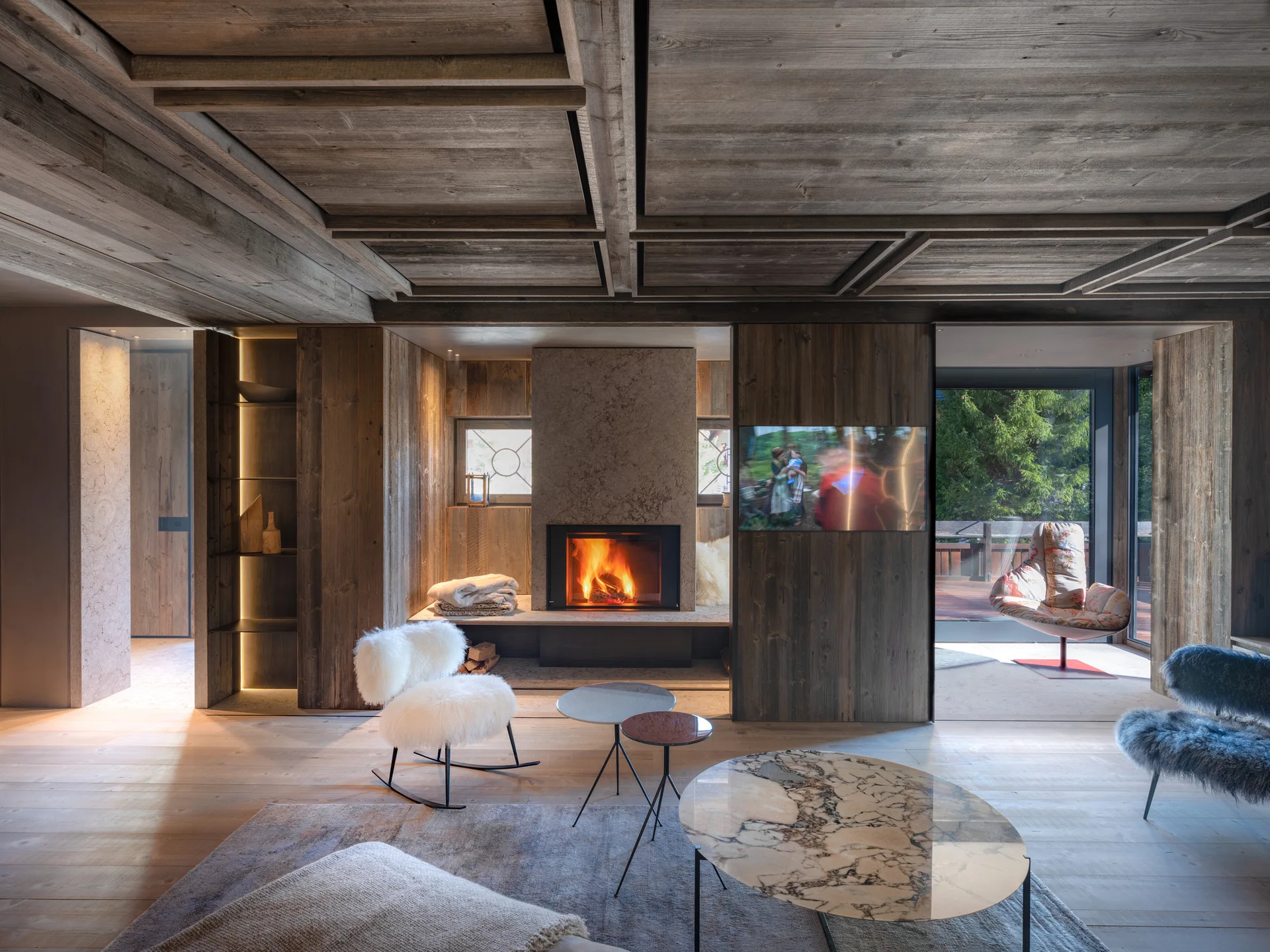A modern alpine living room features warm wood paneled walls and ceiling, a built-in stone fireplace with active flames, and a marble coffee table.