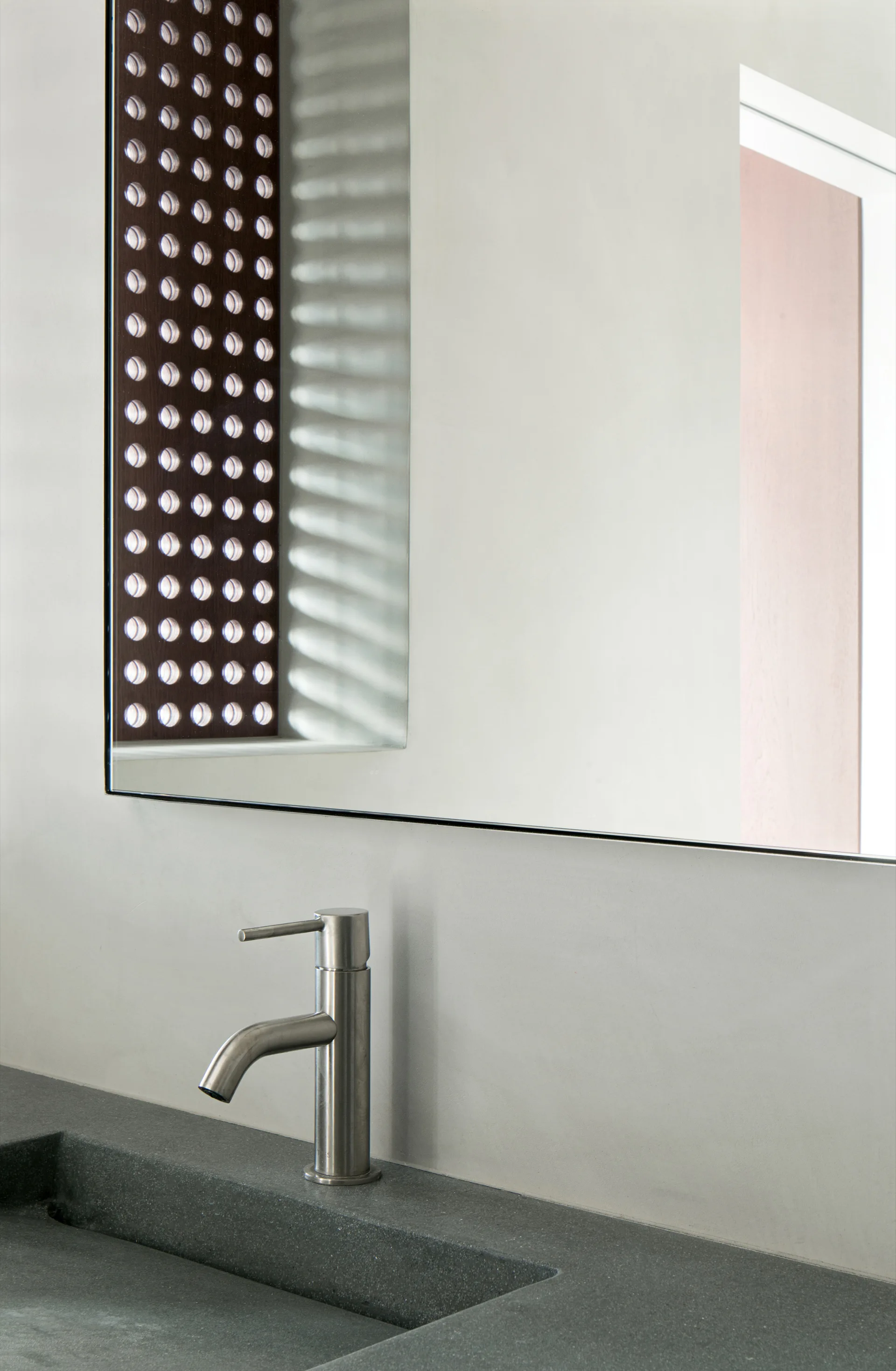 A close-up of a modern bathroom featuring a dark gray stone vanity with an integrated sink, a brushed metal faucet, and a frameless mirror.