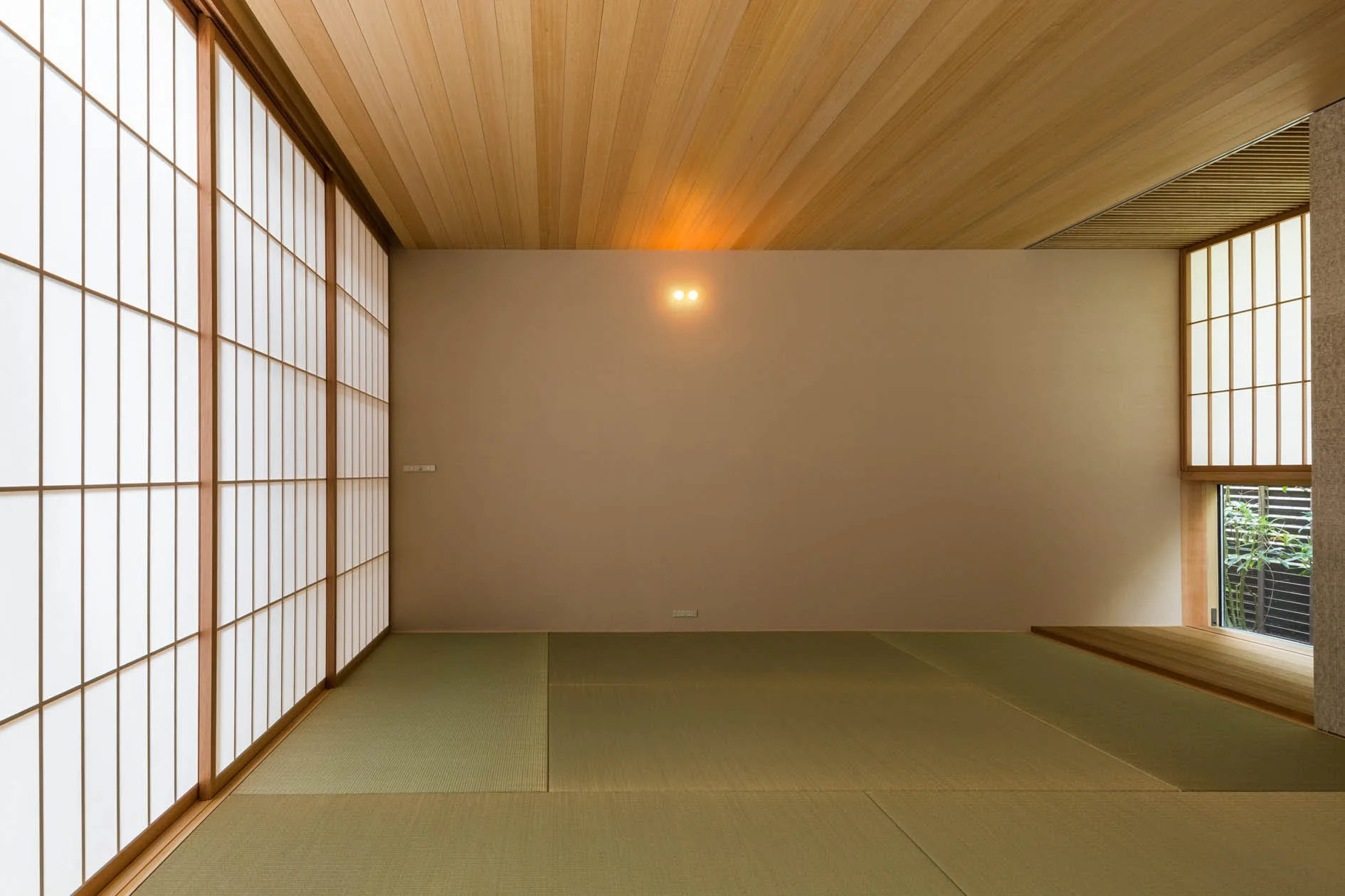 A minimalist Japanese room featuring green tatami mat flooring, a linear wood plank ceiling, and sliding translucent paper shoji screens.