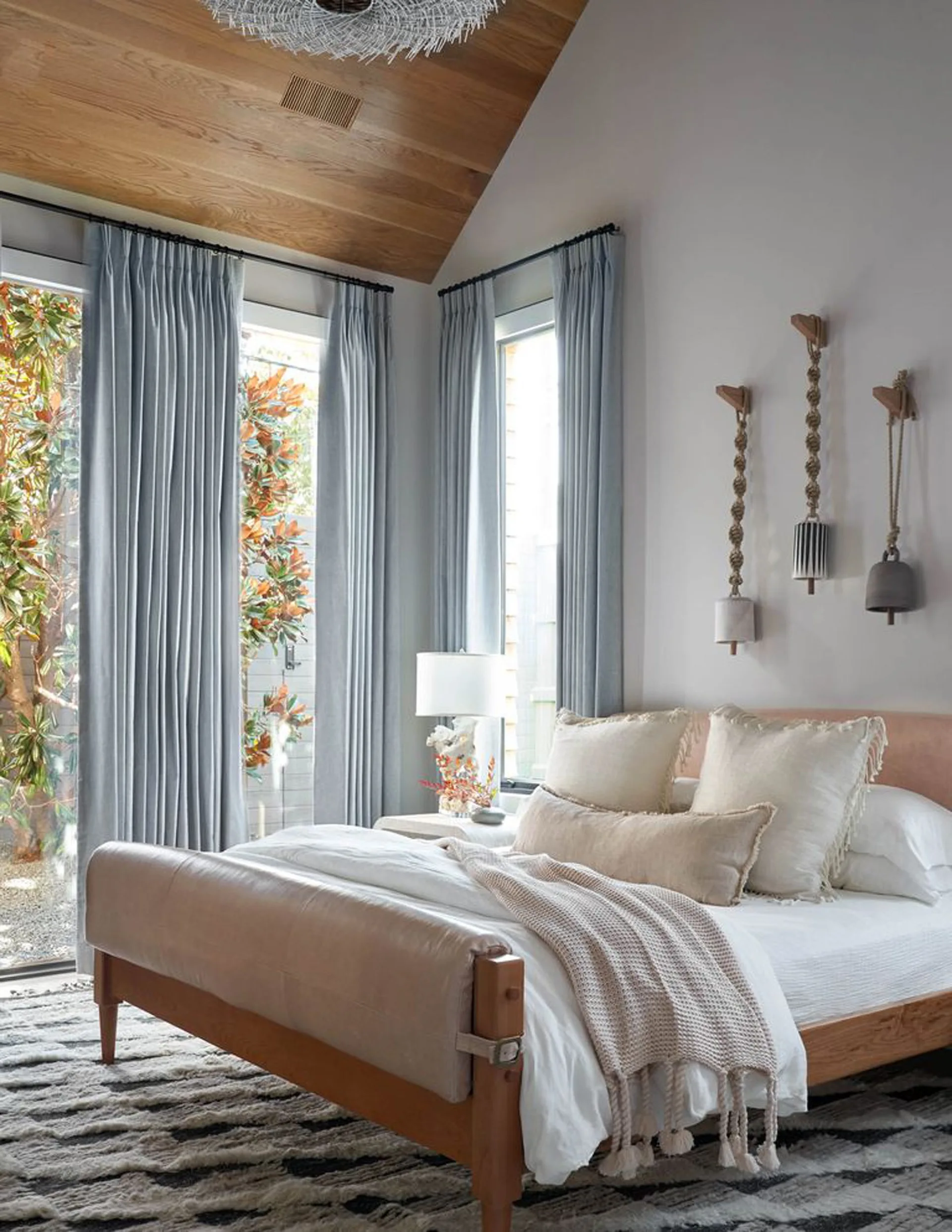 A bedroom with a wooden bed, light blue floor-to-ceiling drapes, and a vaulted wood plank ceiling.