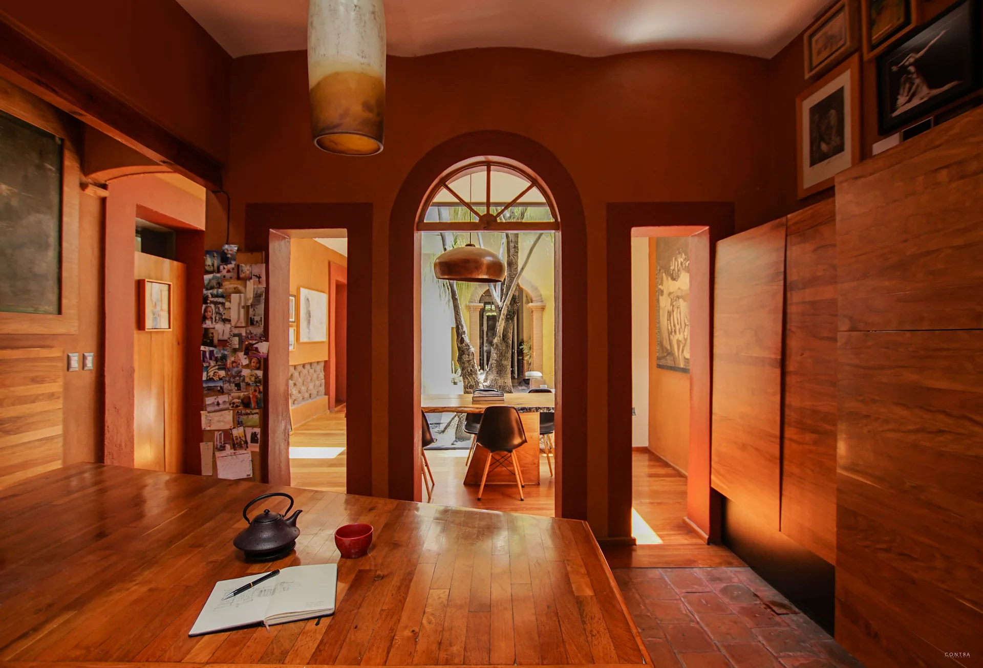 An indoor dining space with terracotta walls and warm wood paneling features a central arched doorway leading to an outdoor courtyard.