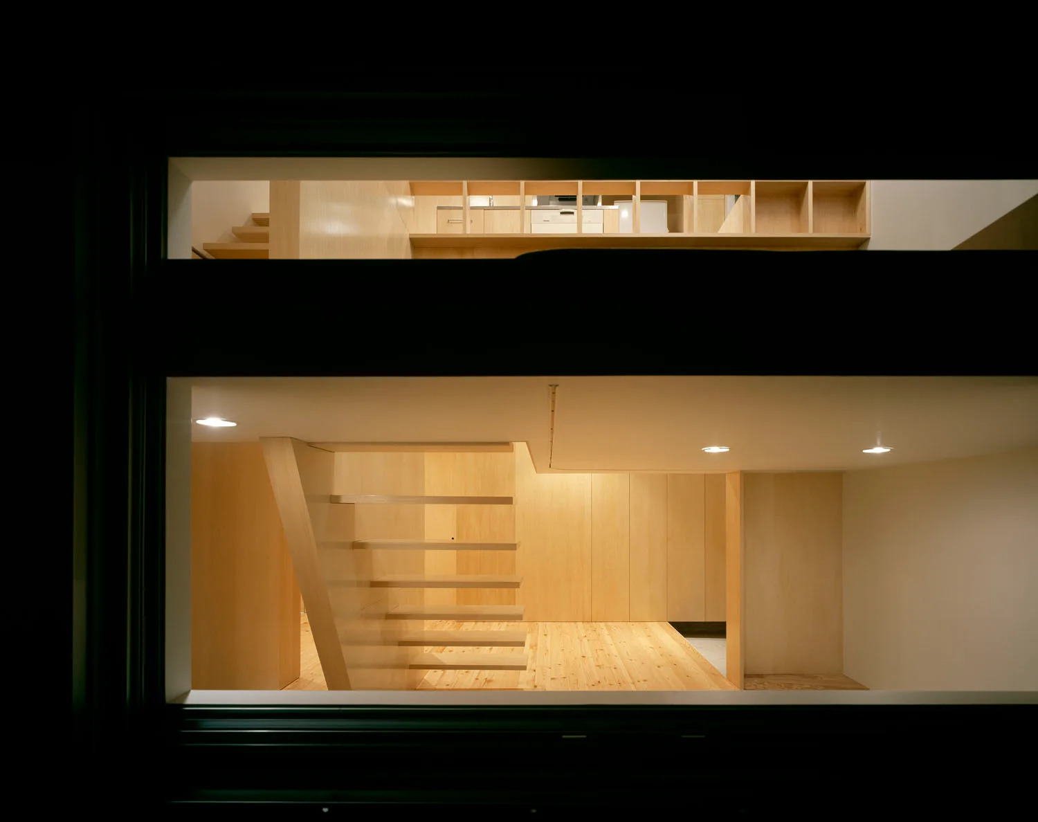 A view through a dark window frame of a modern minimalist interior featuring a light wood floating staircase and integrated upper level shelving.