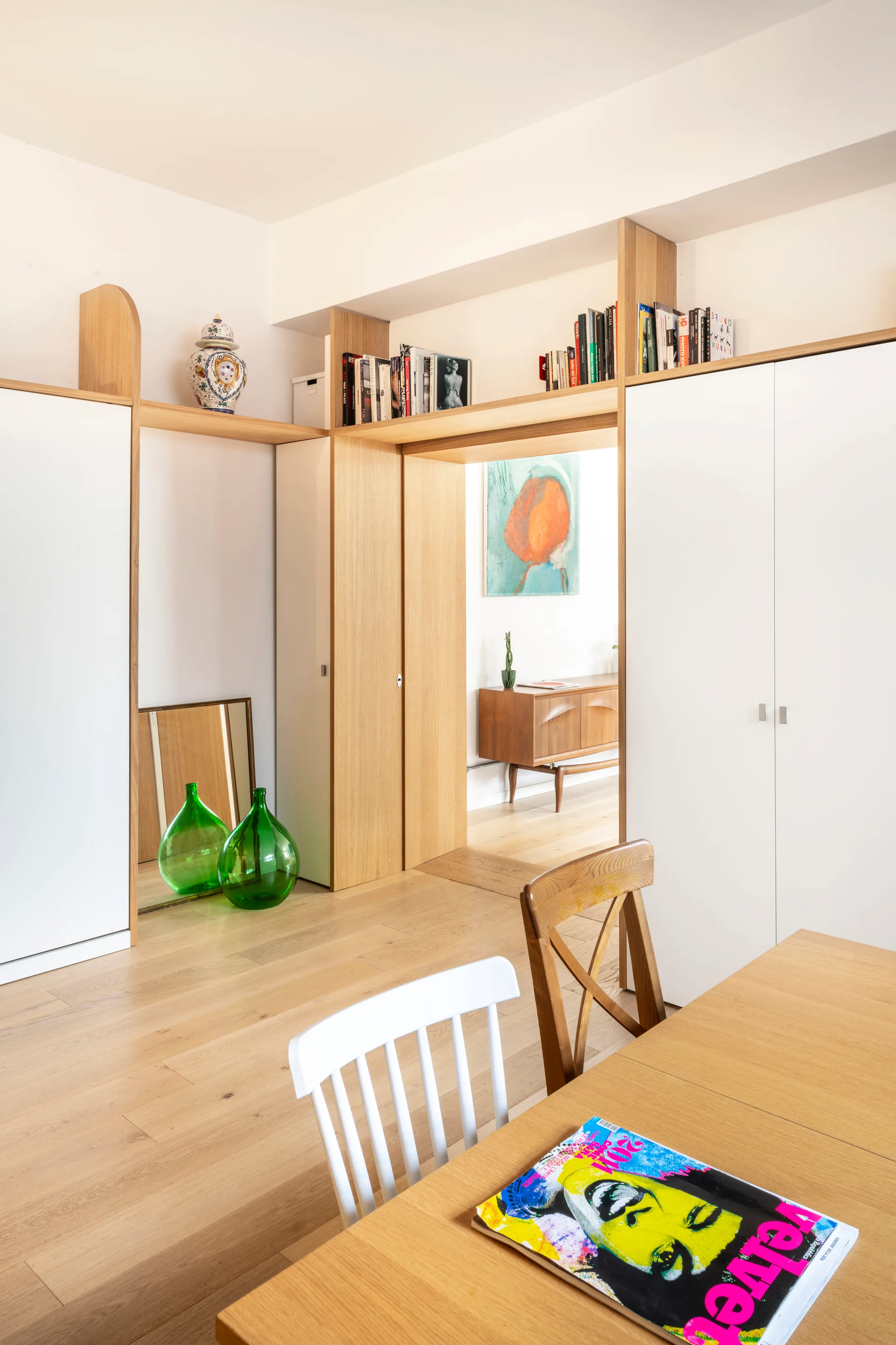 Custom wood-framed white cabinets line a wall and frame an open doorway, with a wood dining table and chair shown in the foreground.