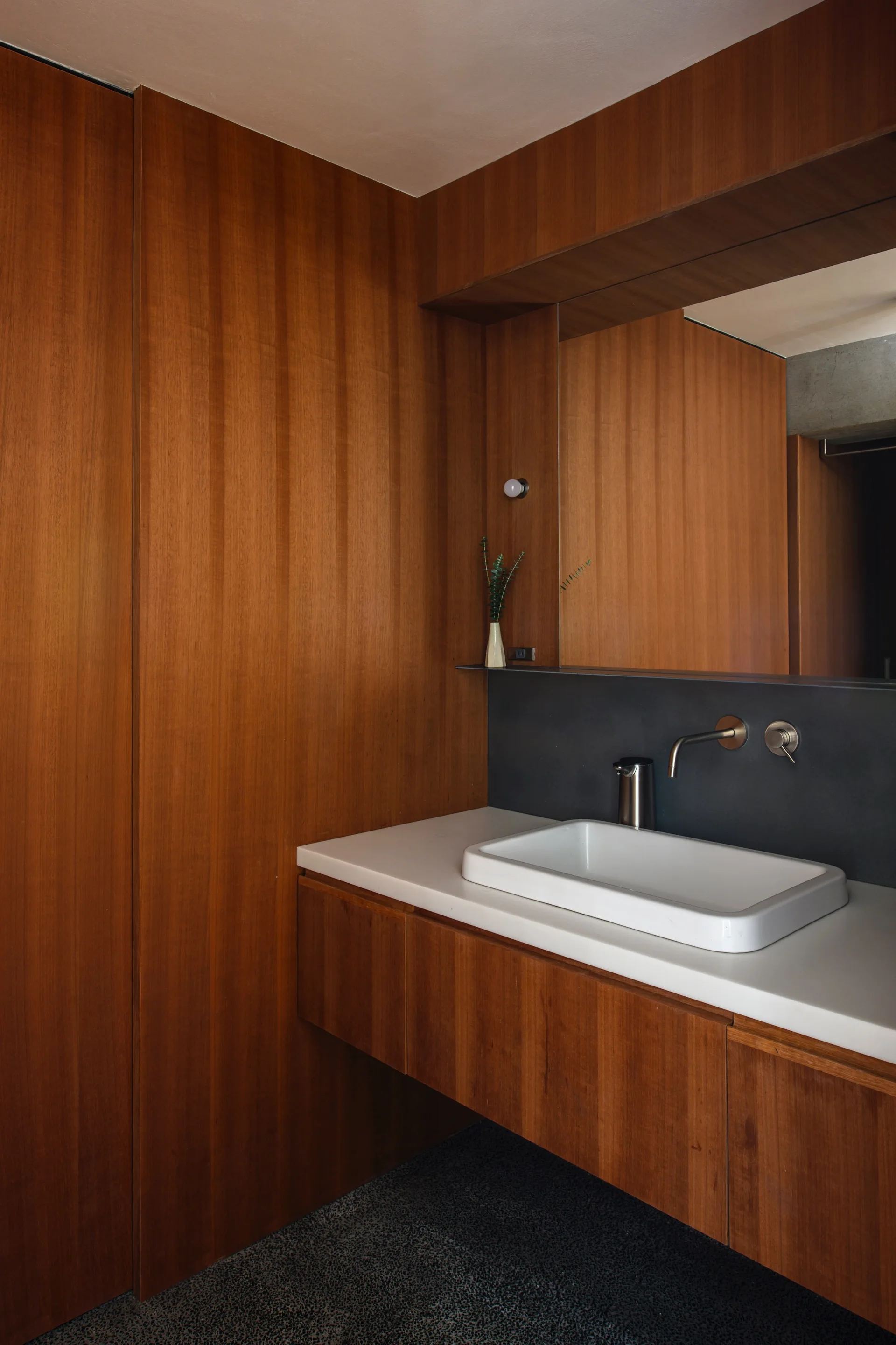 A modern bathroom features a rectangular white sink on a floating wood vanity against matching vertical wood-paneled walls and a large mirror.