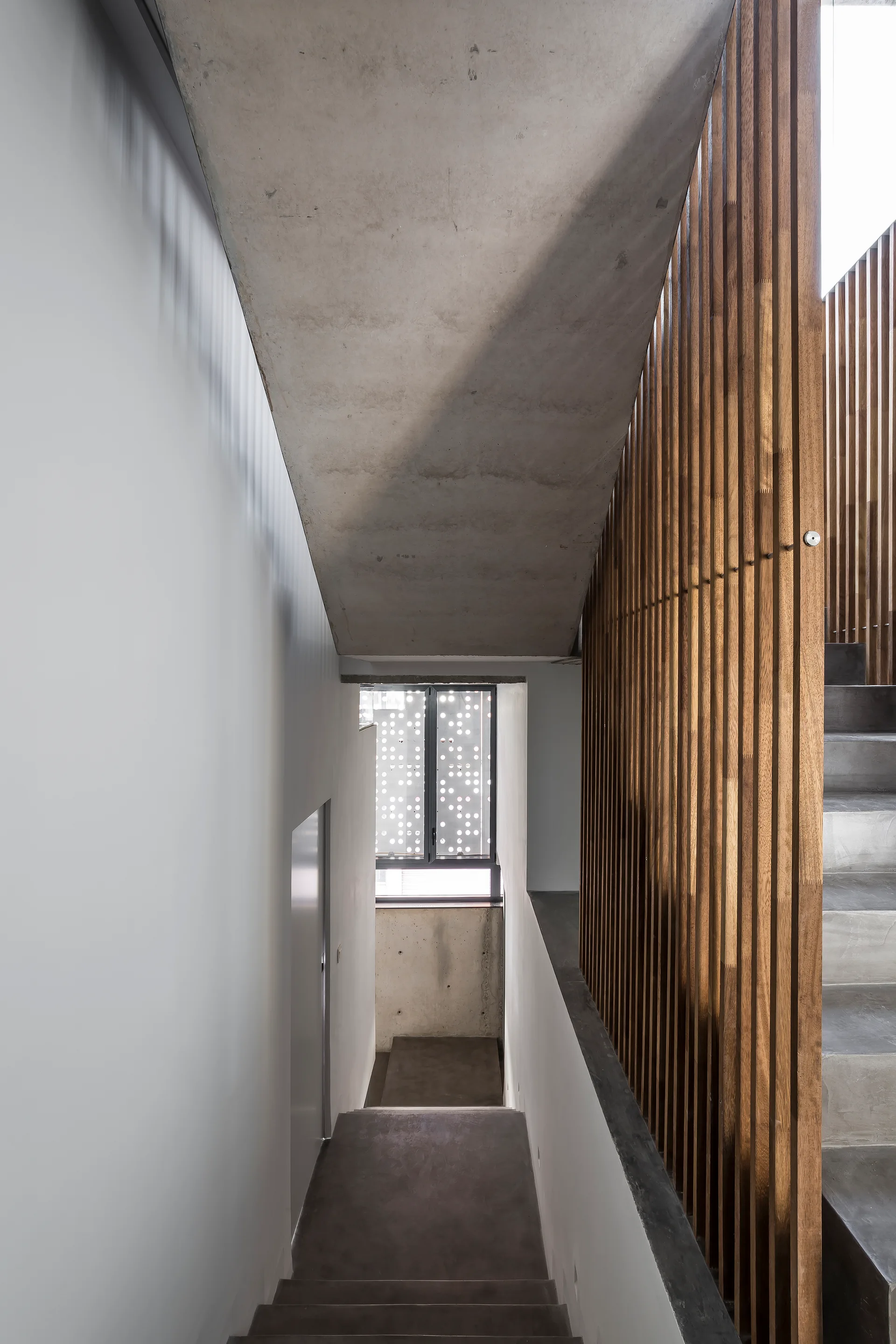 A modern concrete staircase features raw finish steps next to a tall vertical wood slat partition wall under an exposed concrete ceiling.