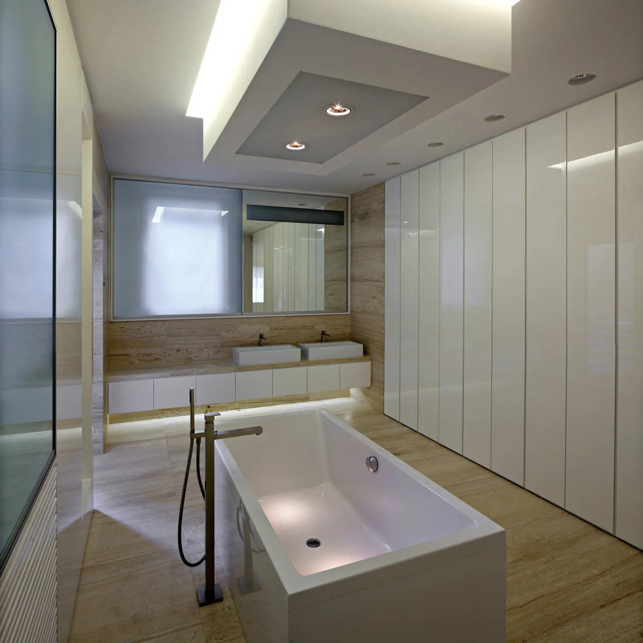 A minimalist bathroom features a freestanding bathtub, floor-to-ceiling glossy white cabinets, and beige stone tile walls with a double vanity.