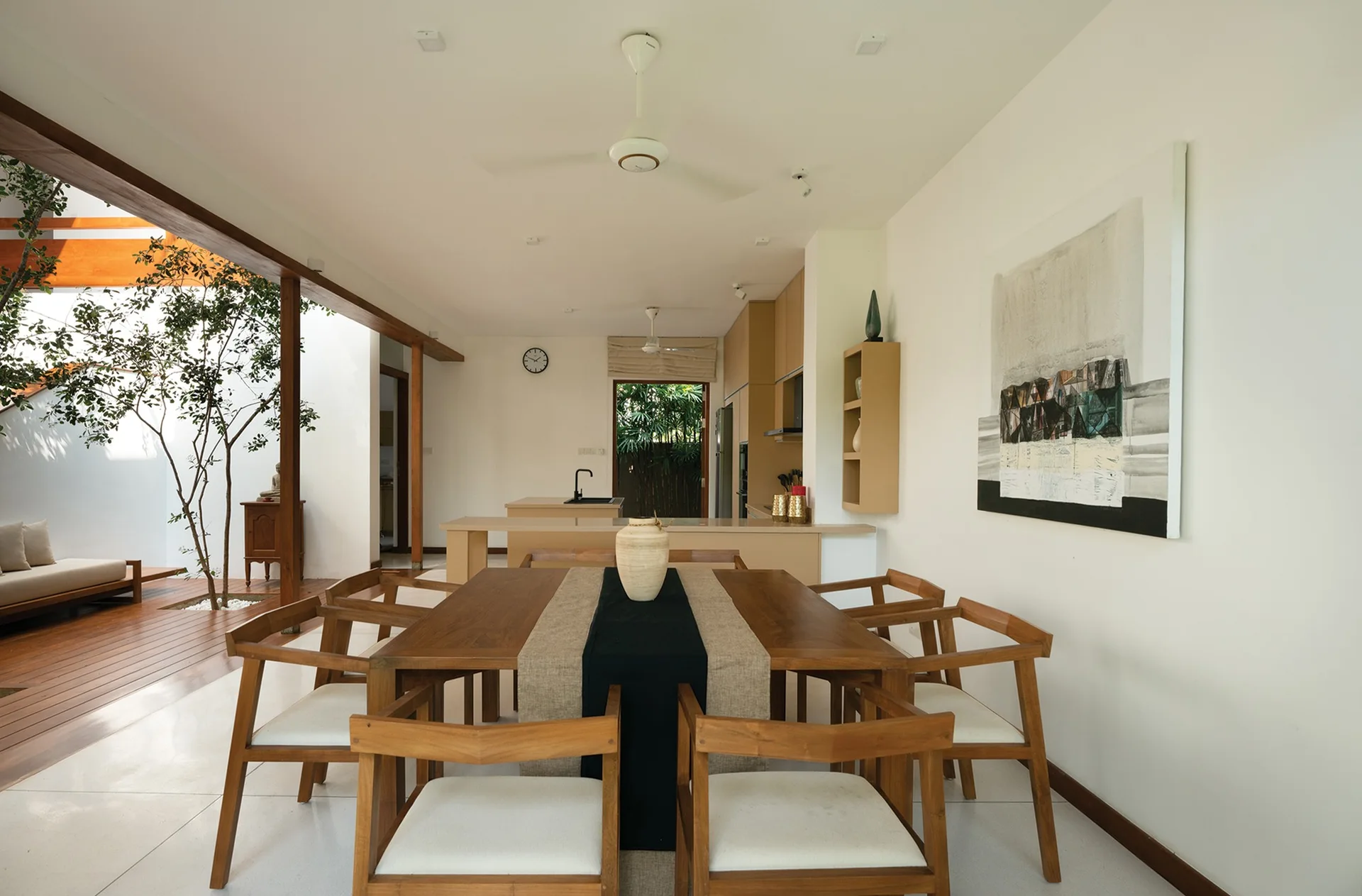 A wooden dining table with six cushioned chairs stands on a white tile floor next to an open doorway leading to a wooden deck.