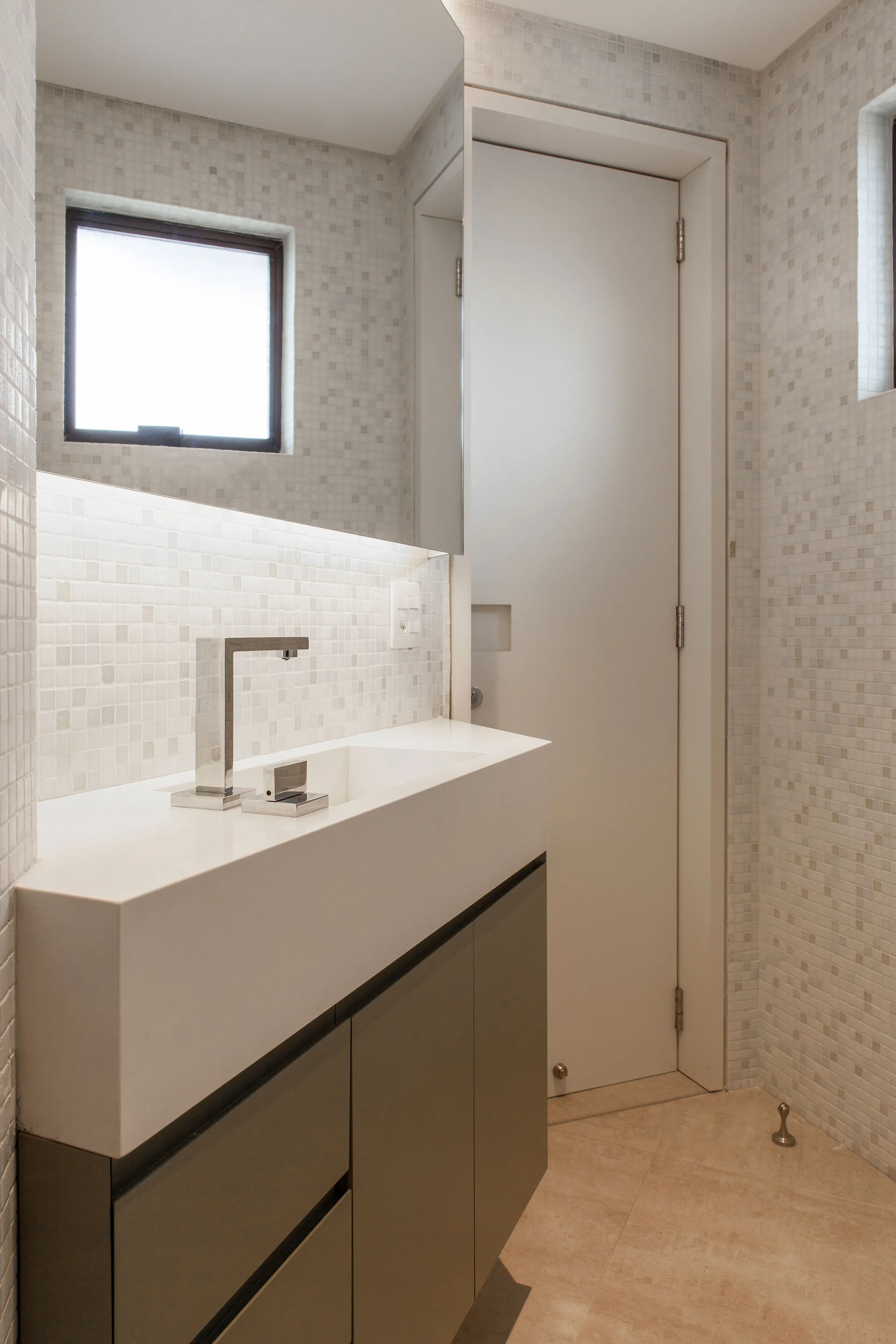 A modern bathroom featuring a grey floating vanity with an integrated white sink, a chrome faucet, and walls covered in light mosaic tiles.