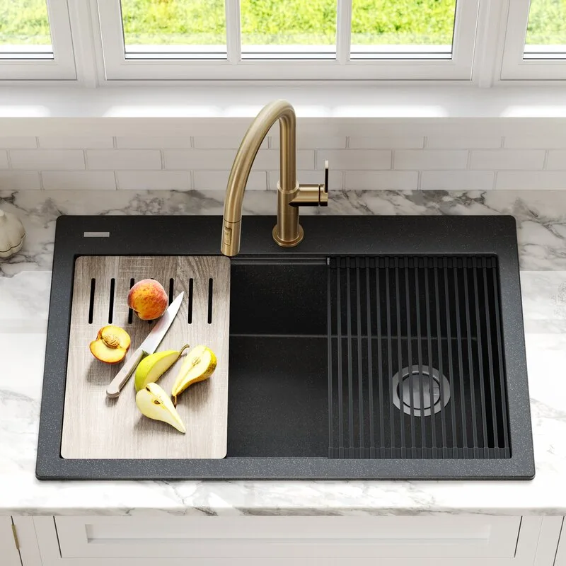 A black workstation kitchen sink with a gold faucet is set in a marbled countertop with a wood cutting board.