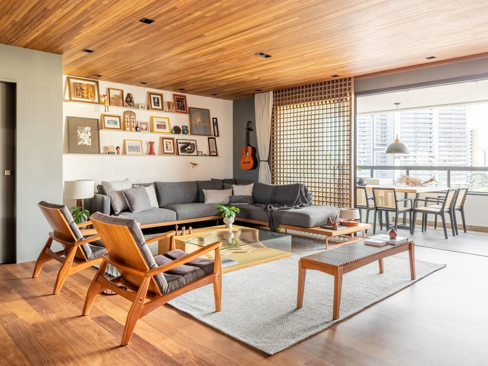 A modern living room featuring a grey sectional sofa, mid-century wood armchairs, a wood plank ceiling, and a wooden lattice partition screen.