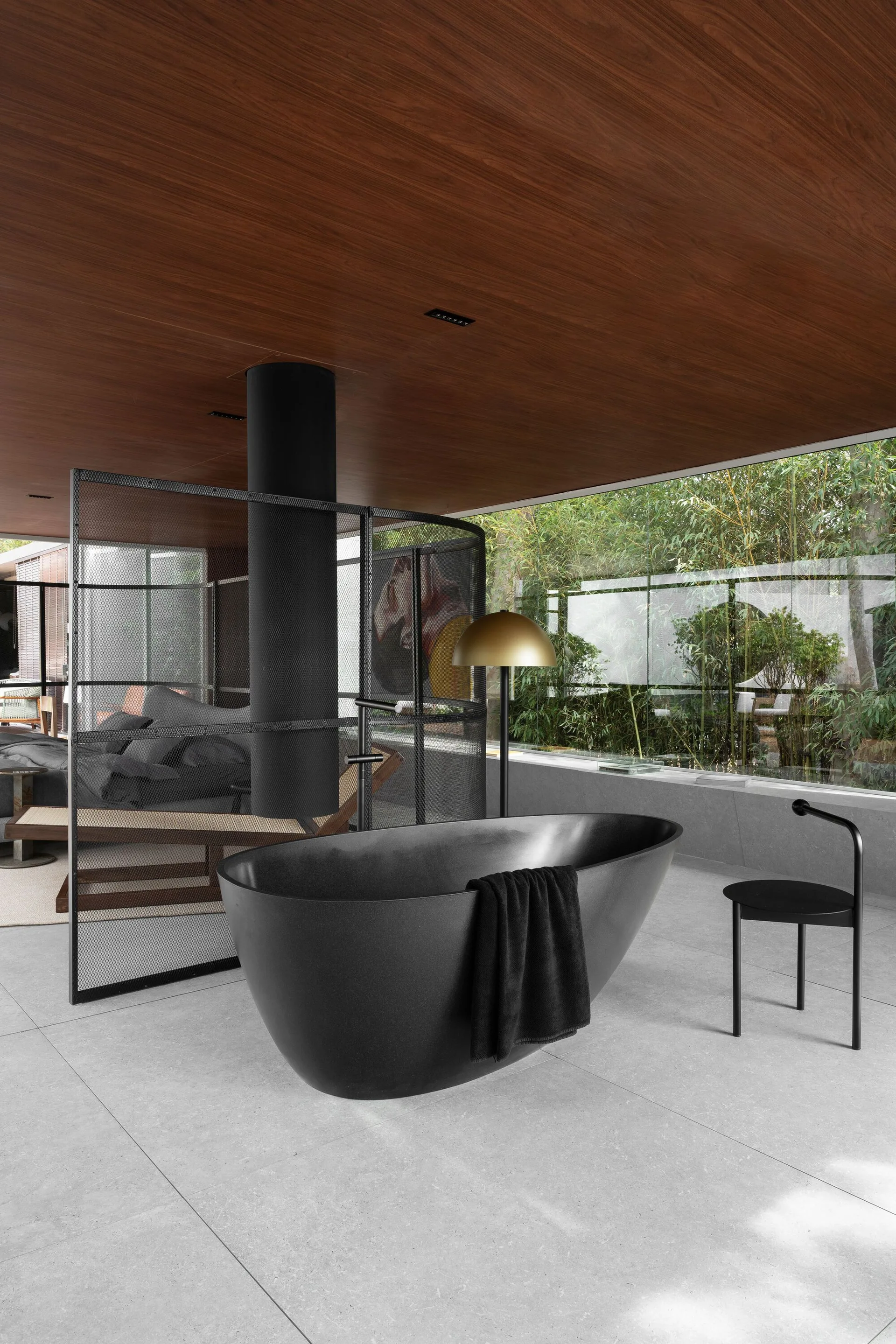 A modern bathroom features a freestanding matte black bathtub, a curved black metal mesh screen, and a warm wood plank ceiling.