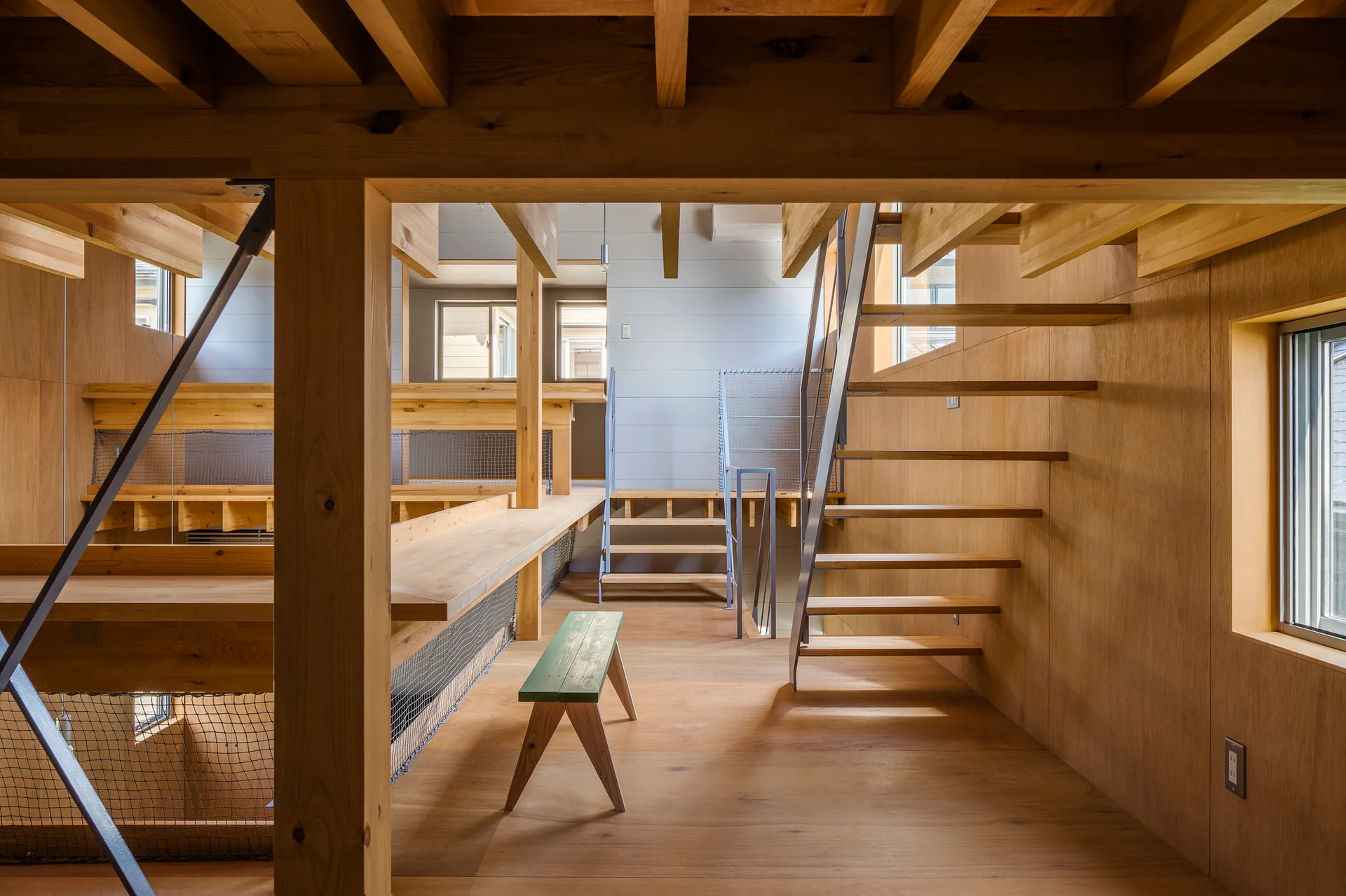 A multi-level interior built from light plywood features an open-riser staircase, exposed ceiling beams, and a green wooden bench.