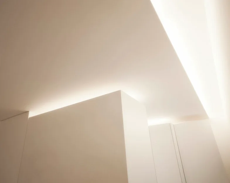 Minimalist white architectural ceiling planes and walls illuminated by warm indirect cove lighting hidden behind recessed edges.