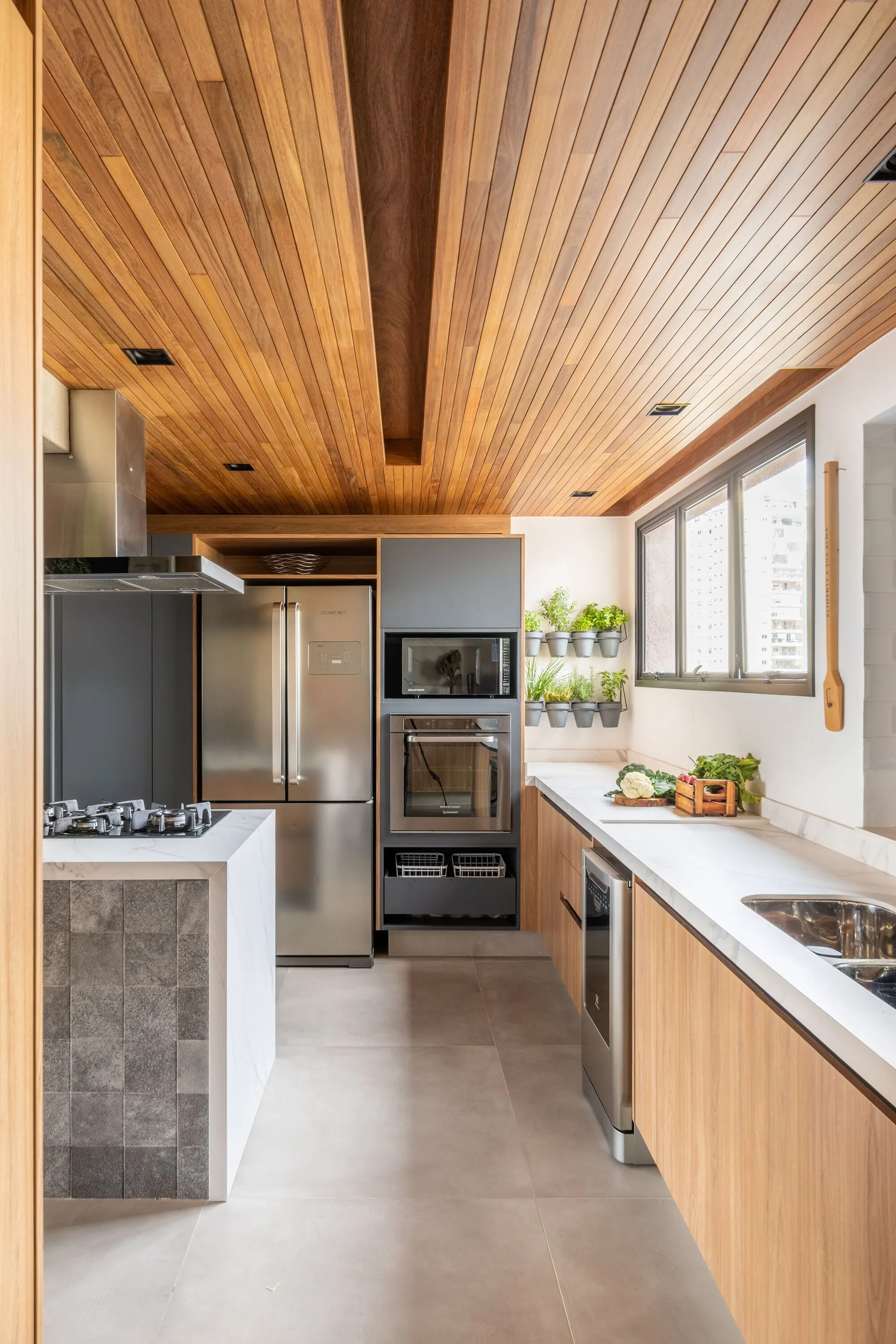 A modern kitchen featuring a wood slatted ceiling, flat-panel wood base cabinets, matte grey tall cabinets, and a waterfall island.