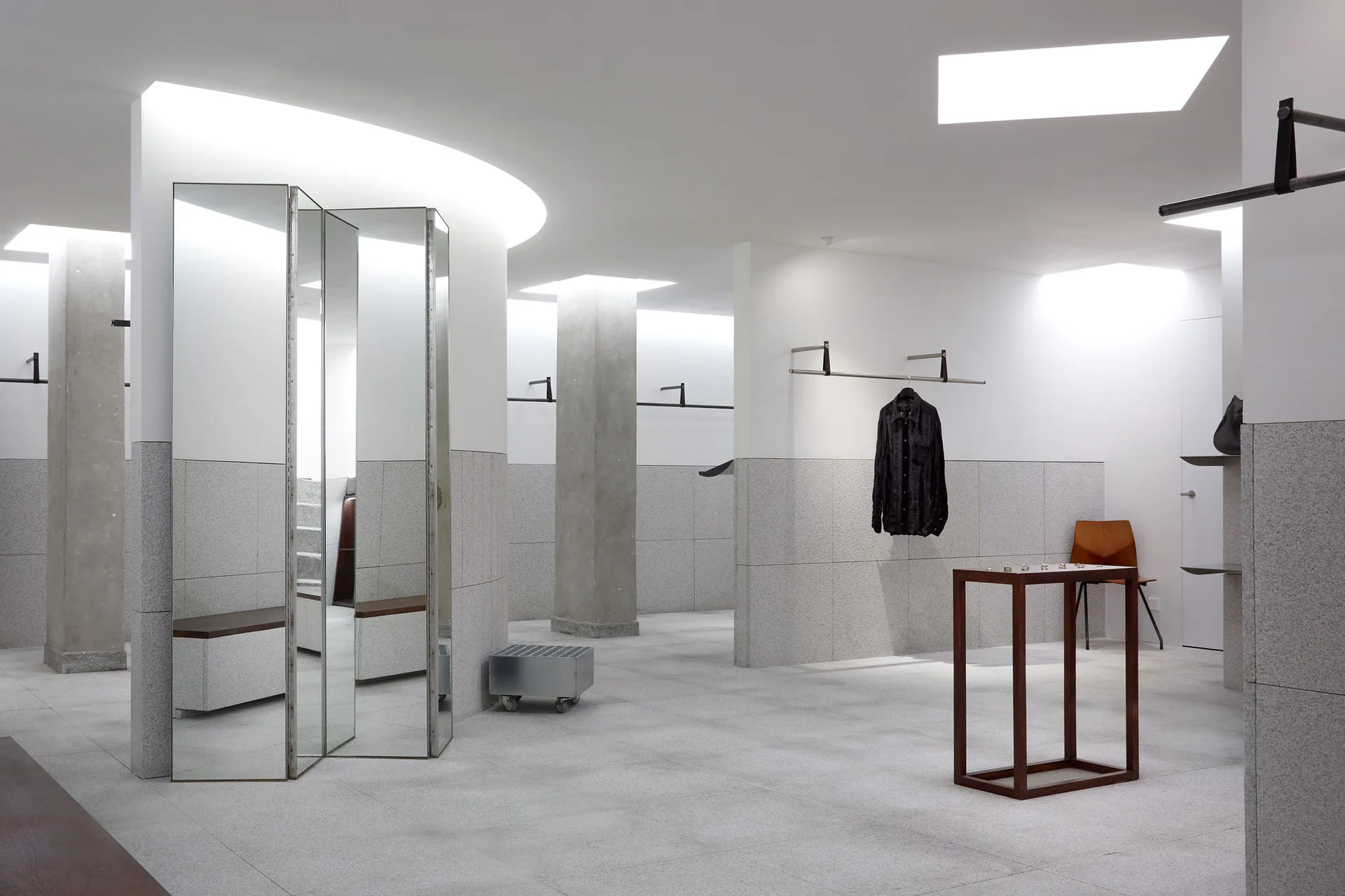 A minimalist retail showroom featuring concrete-clad walls, architectural structural columns, and recessed ceiling cove lighting.