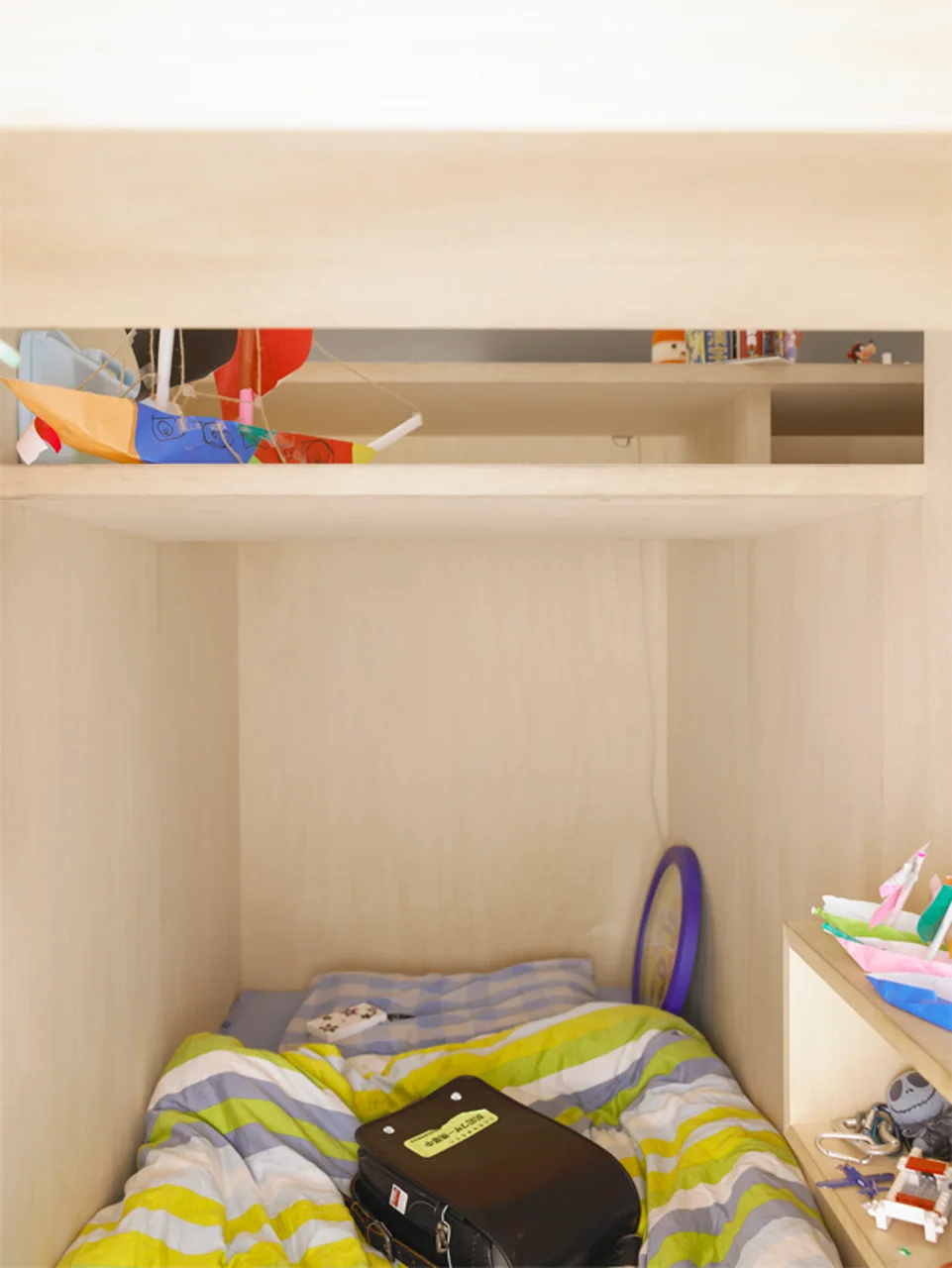 A close-up view of a built-in wooden sleeping nook for kids featuring colorful striped bedding, integrated shelves, and handmade paper crafts.