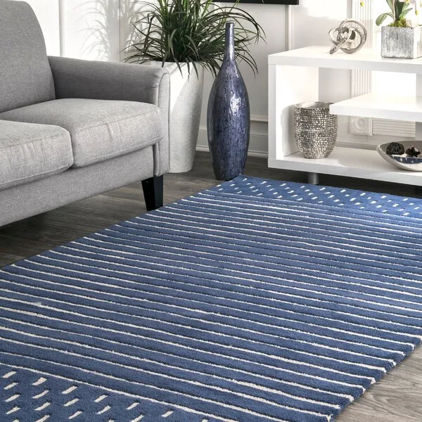 A grey sofa rests on a blue and white striped area rug next to a white console table decorated with metallic sculptures.