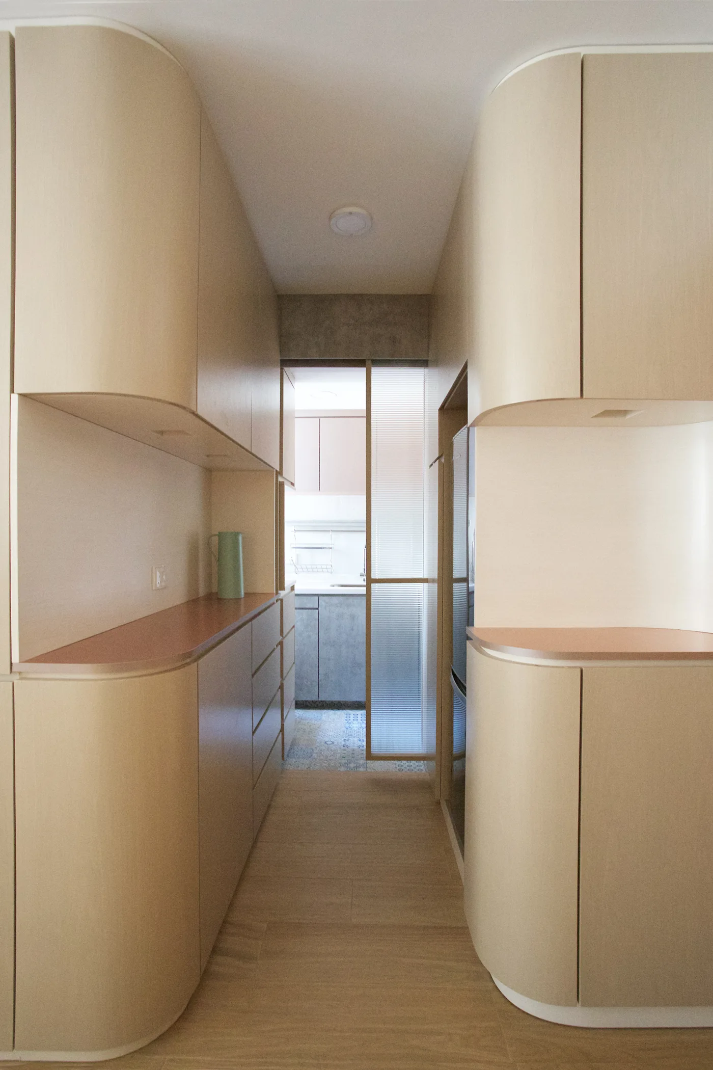 A narrow hallway features custom light wood built-in cabinets with rounded corners and a fluted glass partition door.