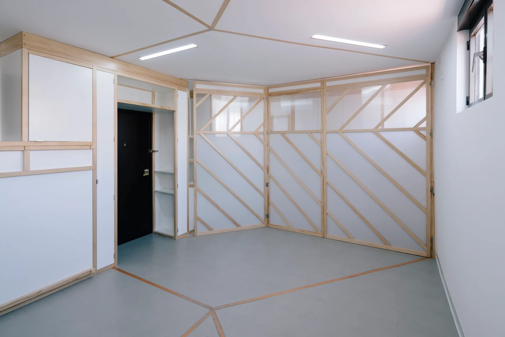 A minimalist white room featuring a custom light wood partition screen with diagonal framing panels and integrated ceiling trim.