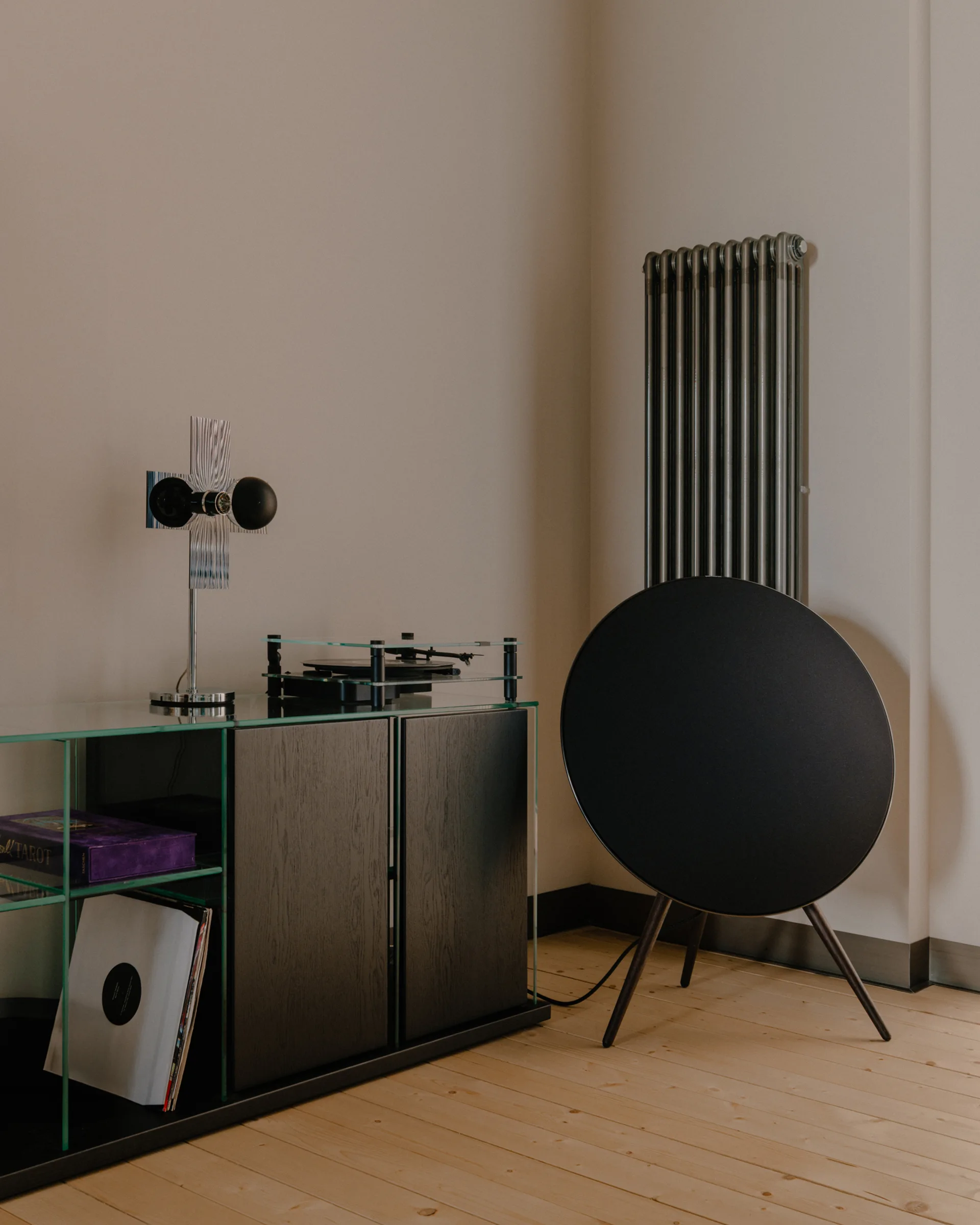 A minimalist corner features a glass and black wood console with a turntable, a circular floor speaker, and a dark vertical radiator.
