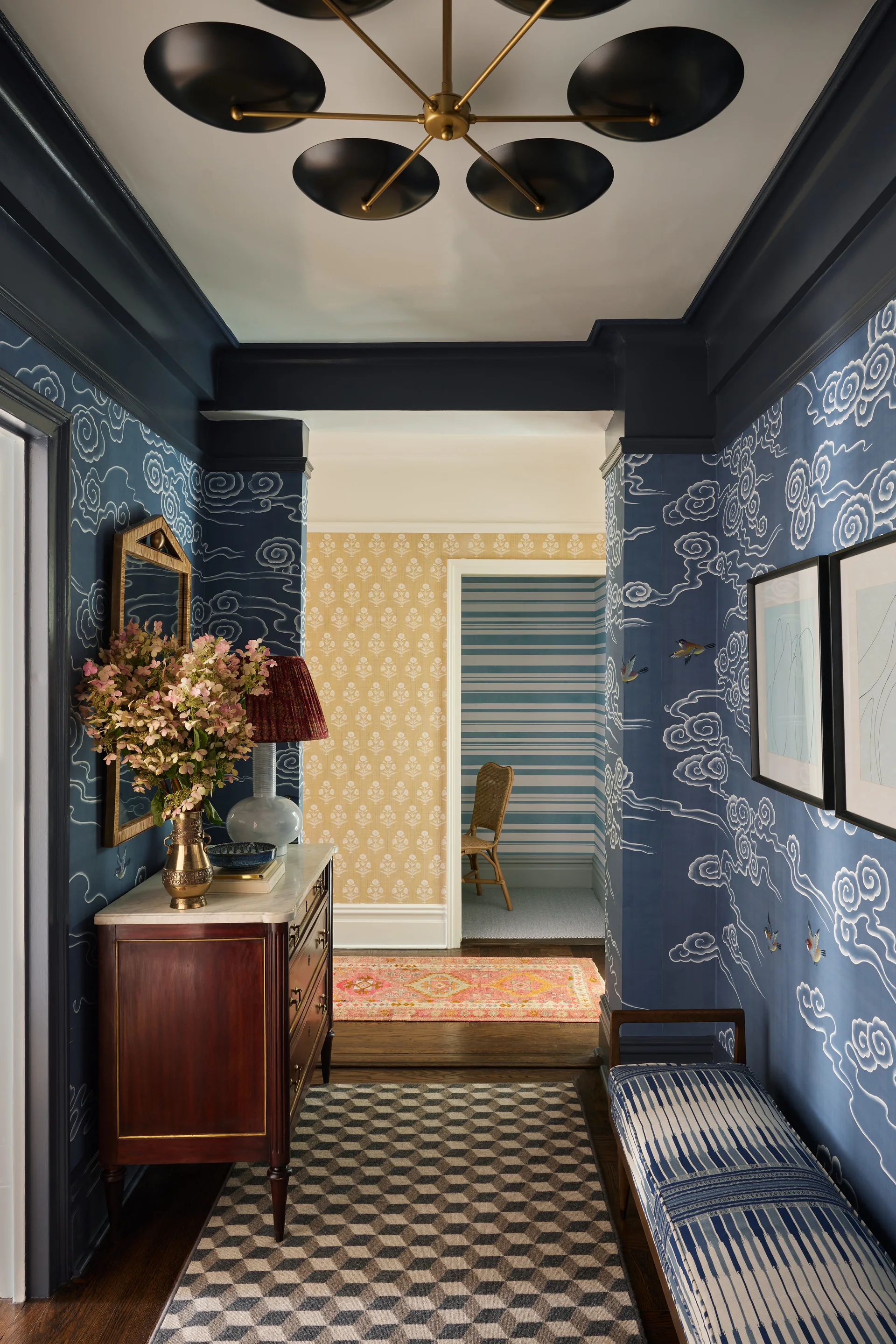 A hallway features blue cloud-patterned wallpaper, a wood console table with a marble top, and a geometric runner rug.