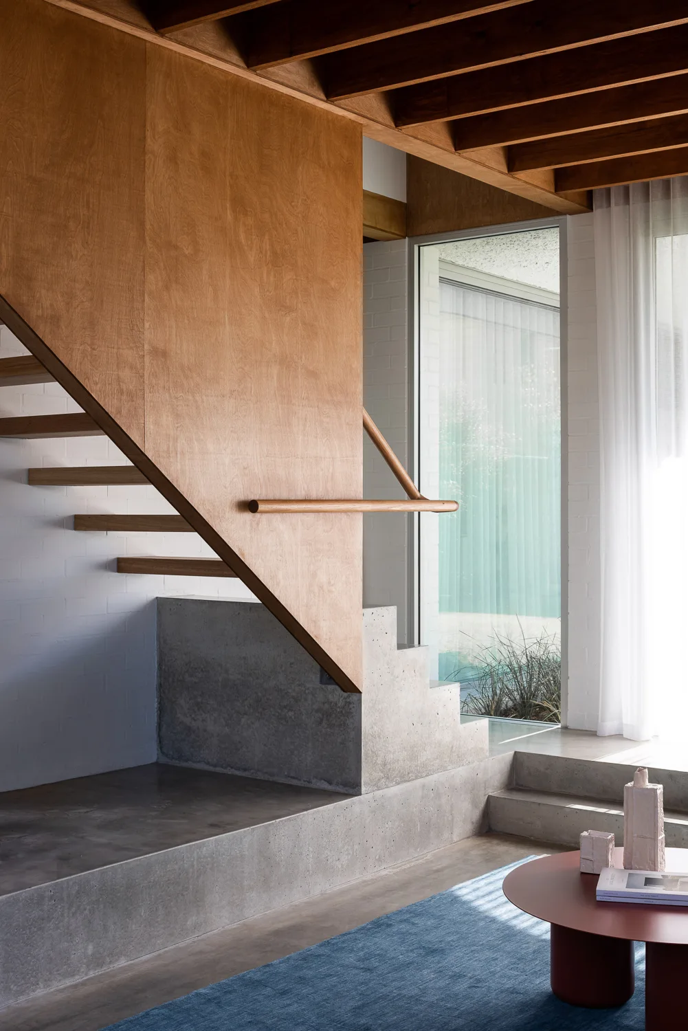 A modern staircase features warm plywood wall panels and a stepped concrete base beneath an exposed timber ceiling.