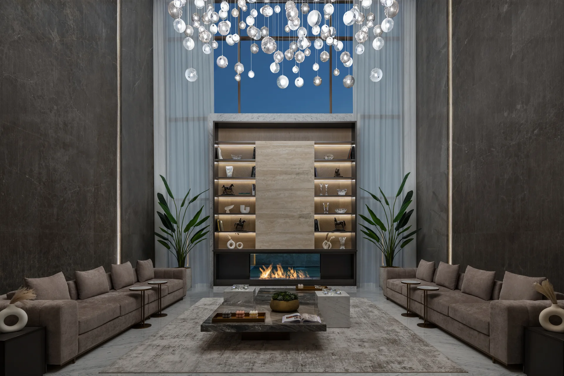 A symmetrical living room featuring two parallel brown sofas, a central marble coffee table, and a built-in fireplace flanked by tall dark walls.