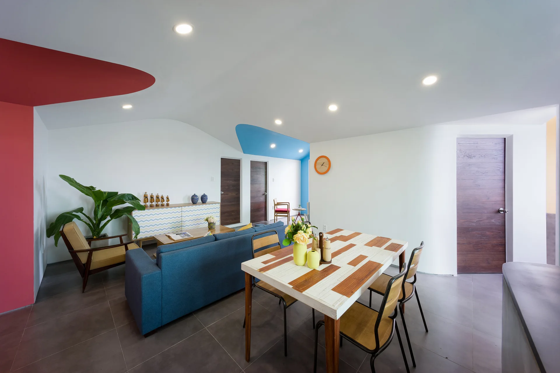 An open-plan living and dining area with a blue sofa, a patterned dining table, and curved walls featuring red and blue painted ceiling details.