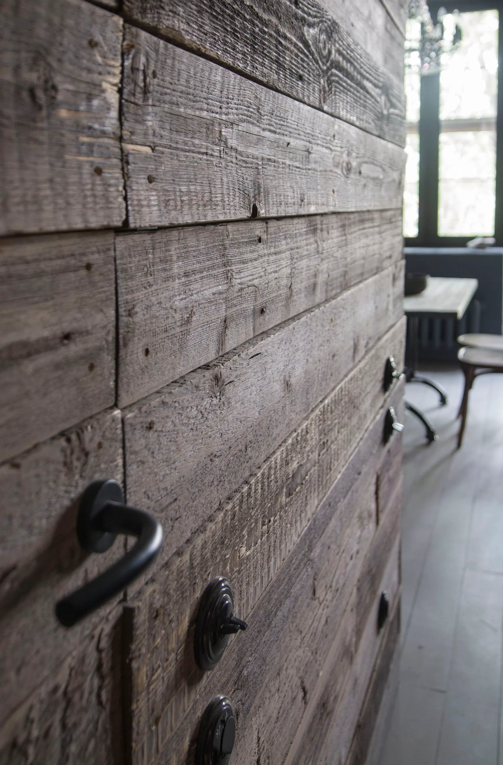 Close-up of weathered reclaimed wood wall paneling featuring a matte black handle and round retro light switches.