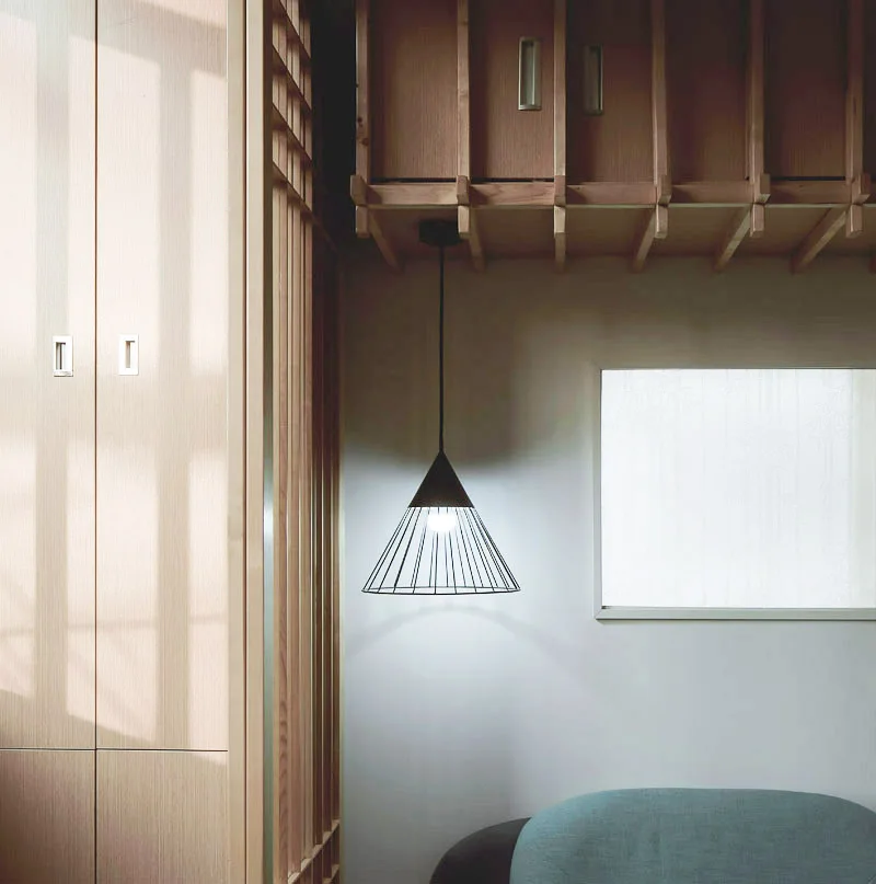 A modern interior features light wood cabinetry, a vertical slat partition, and a black wire cone pendant light hanging in front of a white wall.