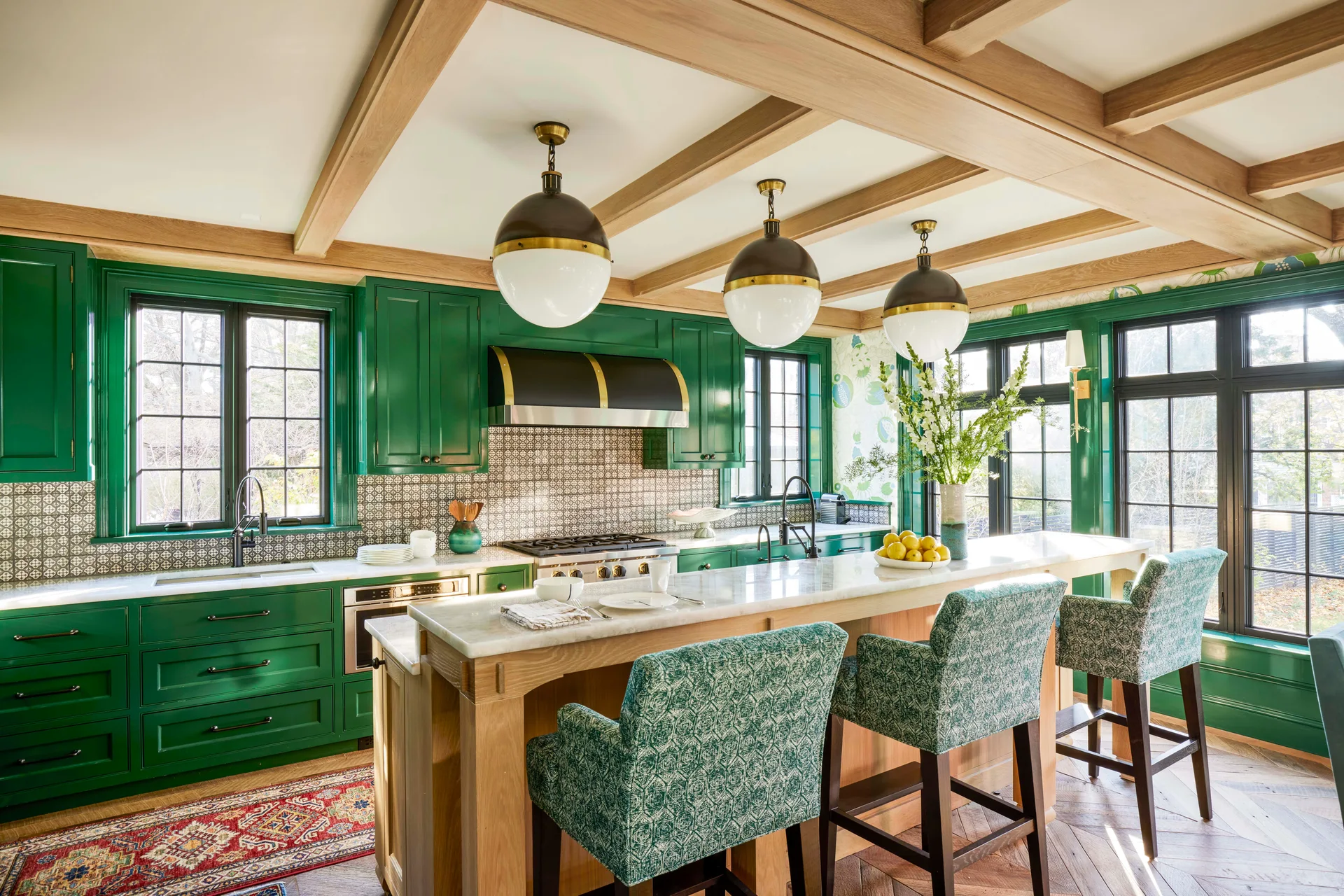 A kitchen featuring glossy emerald green cabinets, a wood-based island with marble countertop, patterned bar stools, and a beamed ceiling.