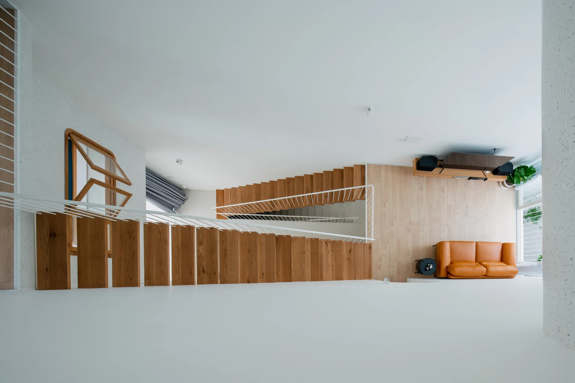 An overhead view looking down a winding wooden staircase with white railings toward a living room featuring an orange leather sofa.
