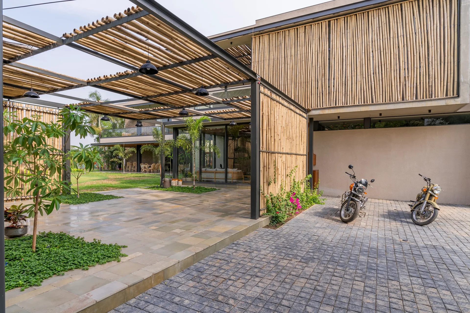 A modern outdoor patio features a black metal pergola topped with bamboo poles, stone flagstone flooring, and a building facade clad in vertical bamboo.