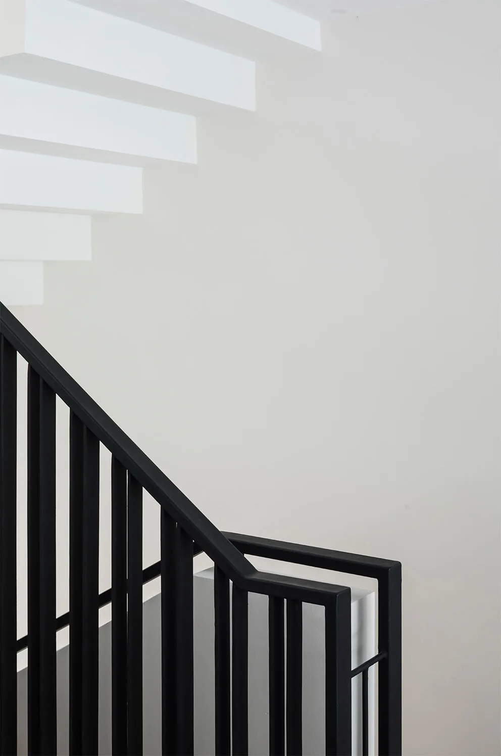 A minimalist staircase features white floating steps and a stark black metal railing against a solid white wall.