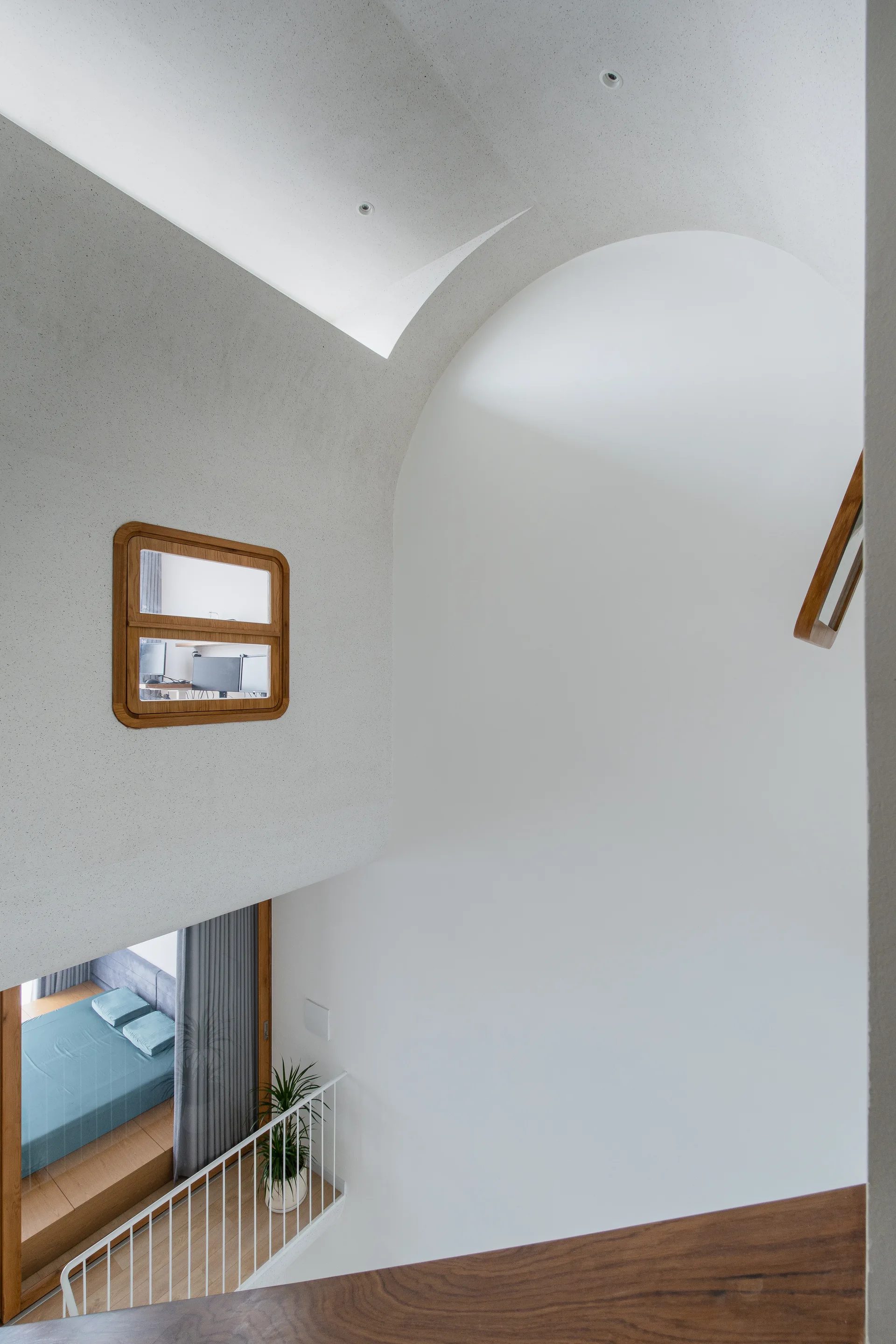 A minimalist staircase landing with curved plaster ceilings, a white metal railing, and a small wood-framed internal window.